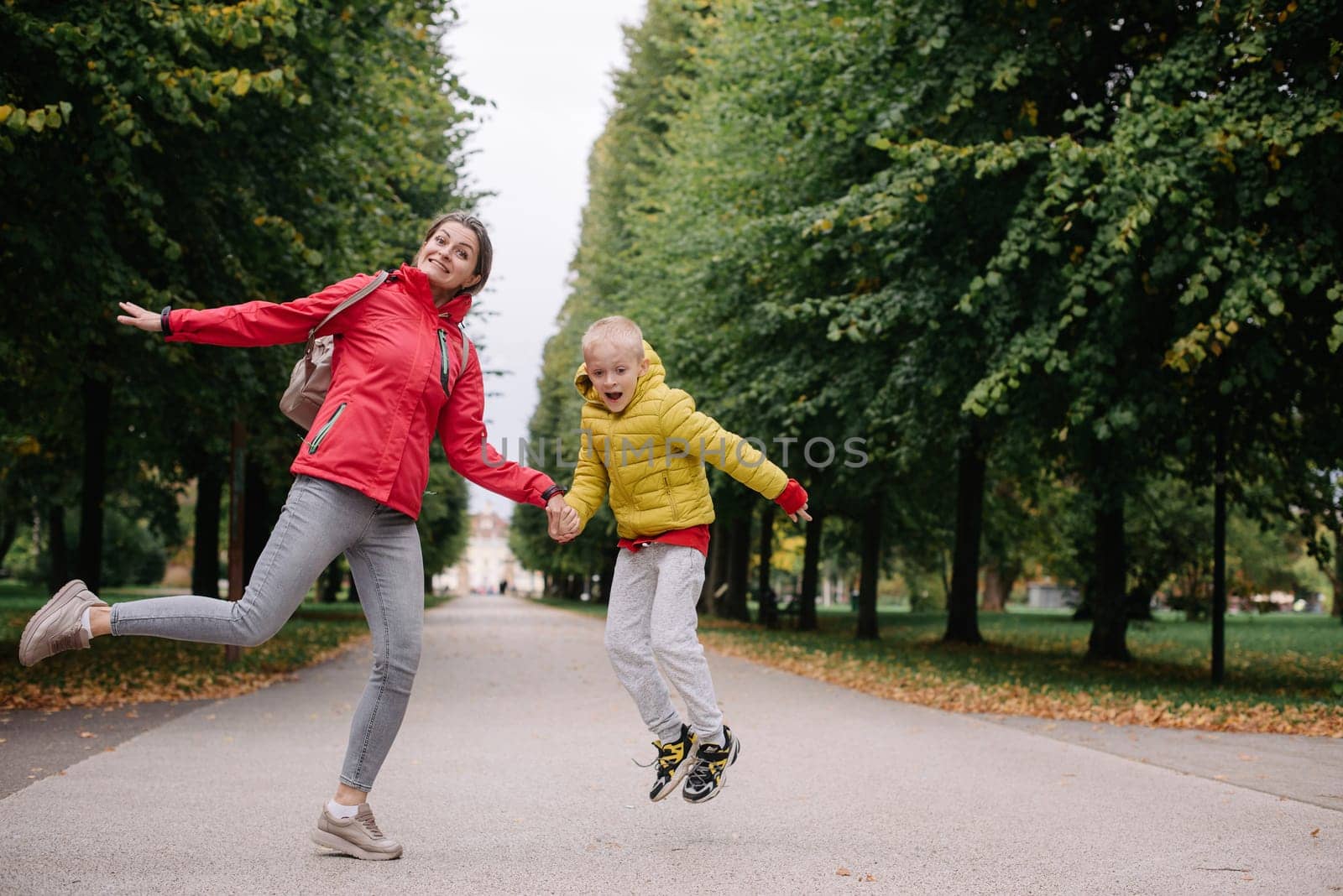 Mother and son jumping in the autumn park. Fall Season. Happy young beautiful mother and her son have a walk in the park