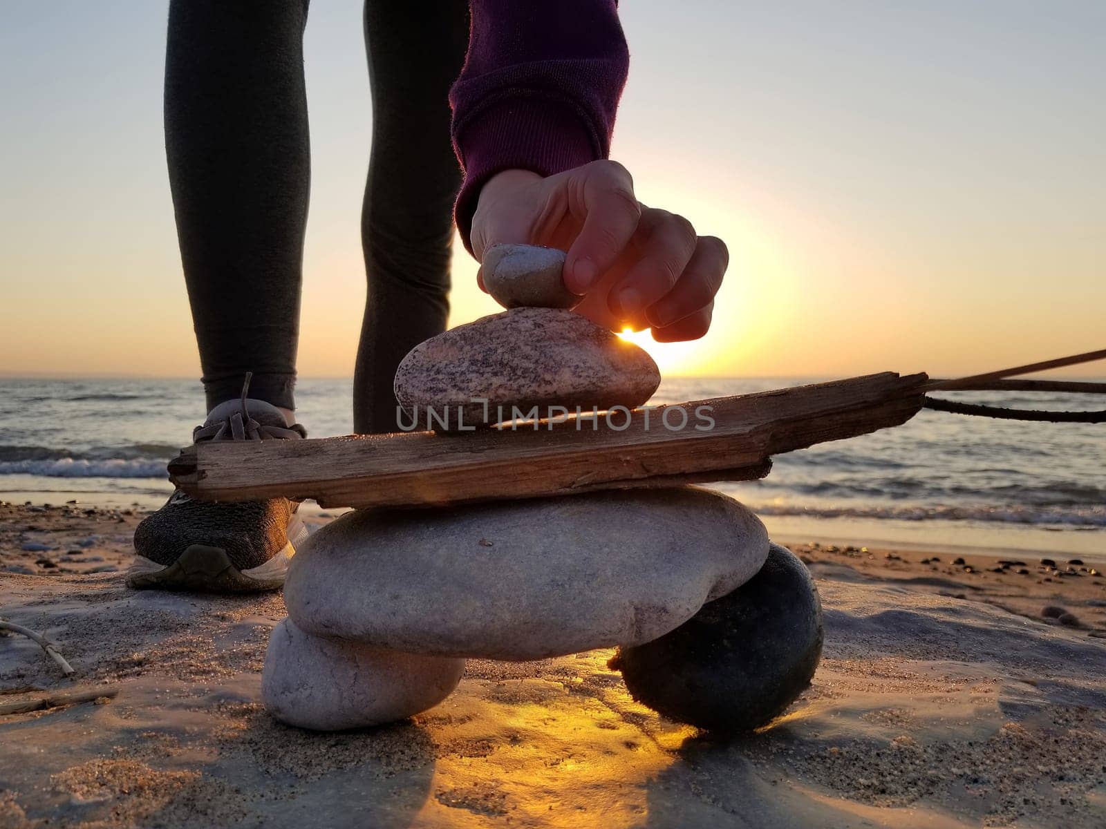 Young girl builds an inukshuk inuksuk with seaweed hair at the beach at sunset 2