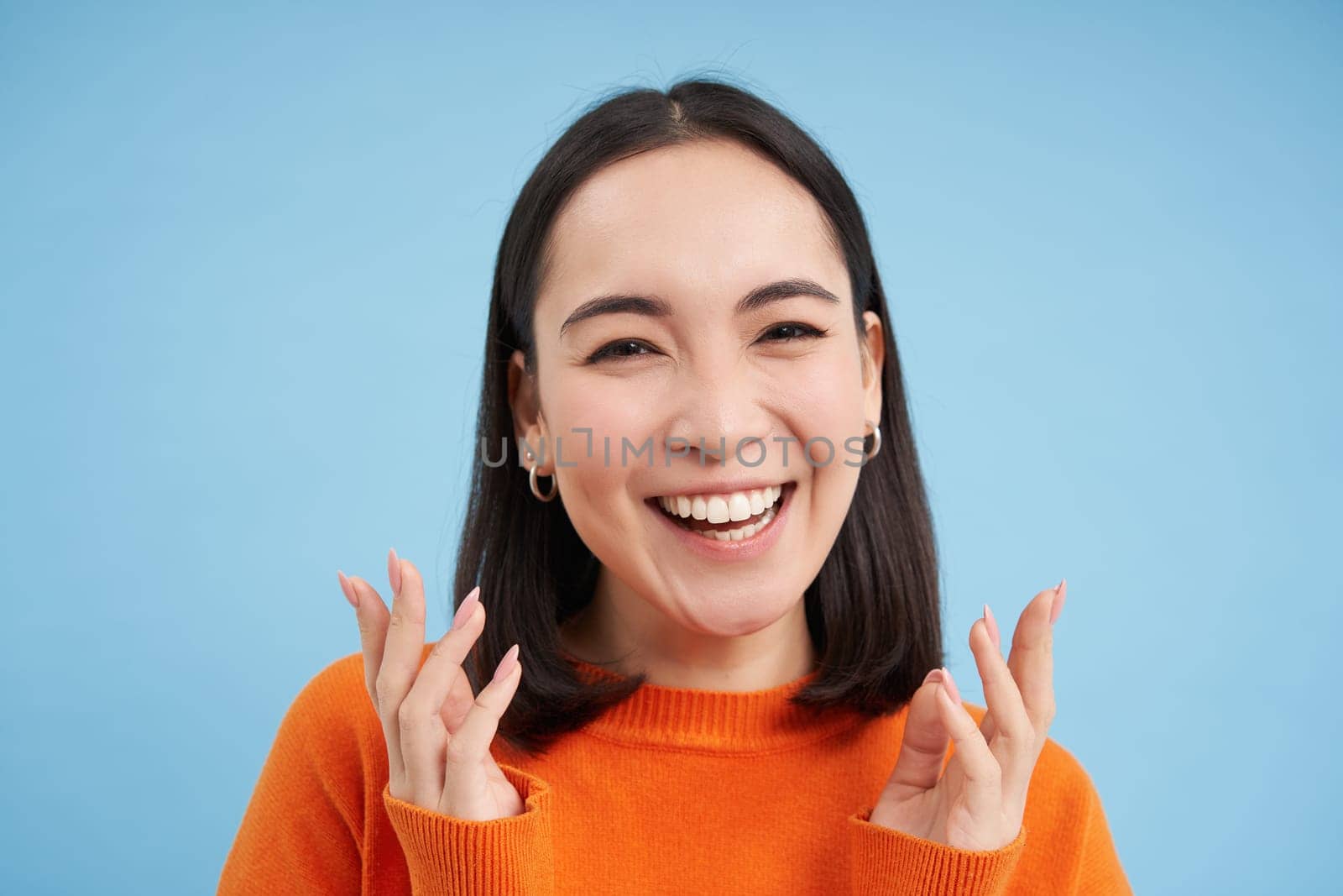 Close up portrait of asian girl with perfect healthy smile and natural beautiful face, looks happy at camera, stands over blue background.