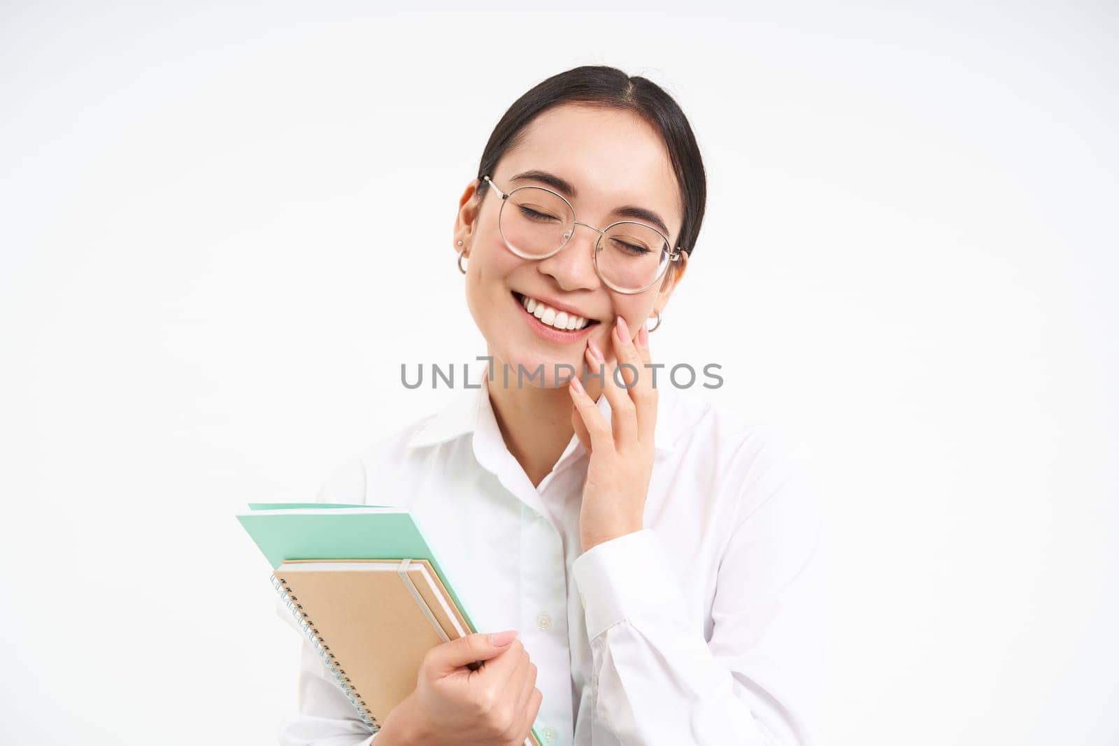 Successful young asian woman, teacher with notebooks, looking confident and smiling, white studio background by Benzoix