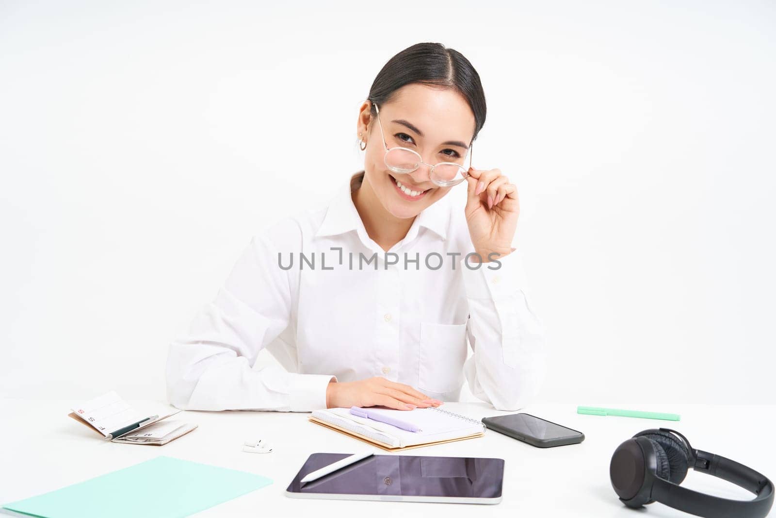 Portrait of successful businesswoman, office manager at workplace, sits with digital tablet and her working documents, wears glasses, smiles at camera by Benzoix