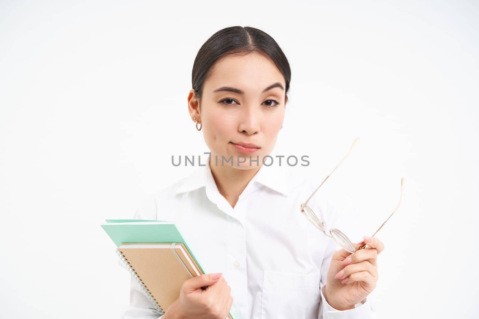 Confident young woman, office worker with glasses, holds notebooks, looks thoughtful, thinking, standing isolated on white background.