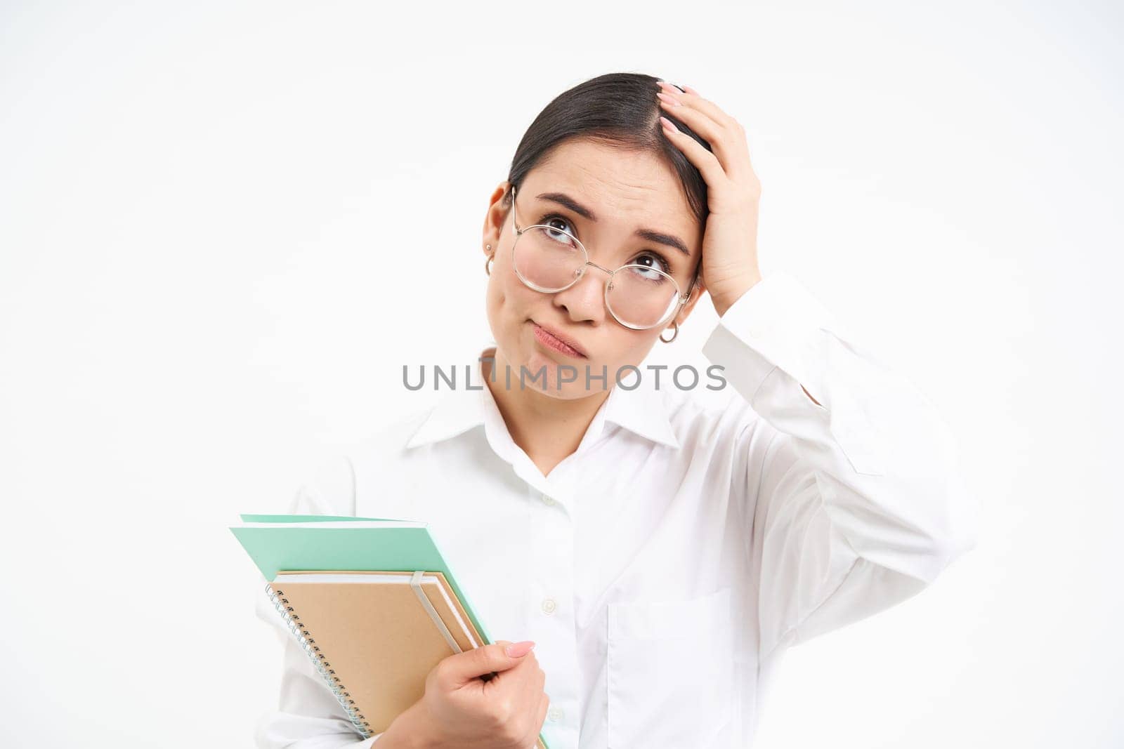 Troubled asian woman, feels complicated, looks upset and frustrated, stands with notebooks over white studio background.