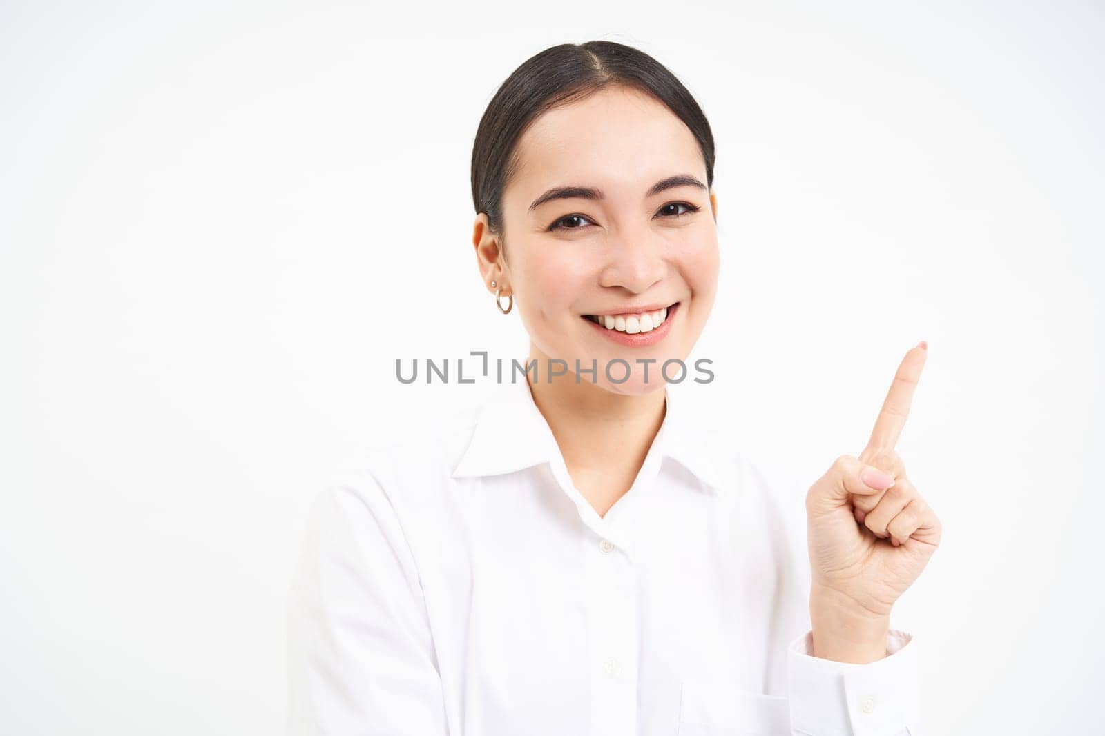 Successful korean businesswoman, pointing finger right, showing advertisement on banner, standing over white background.