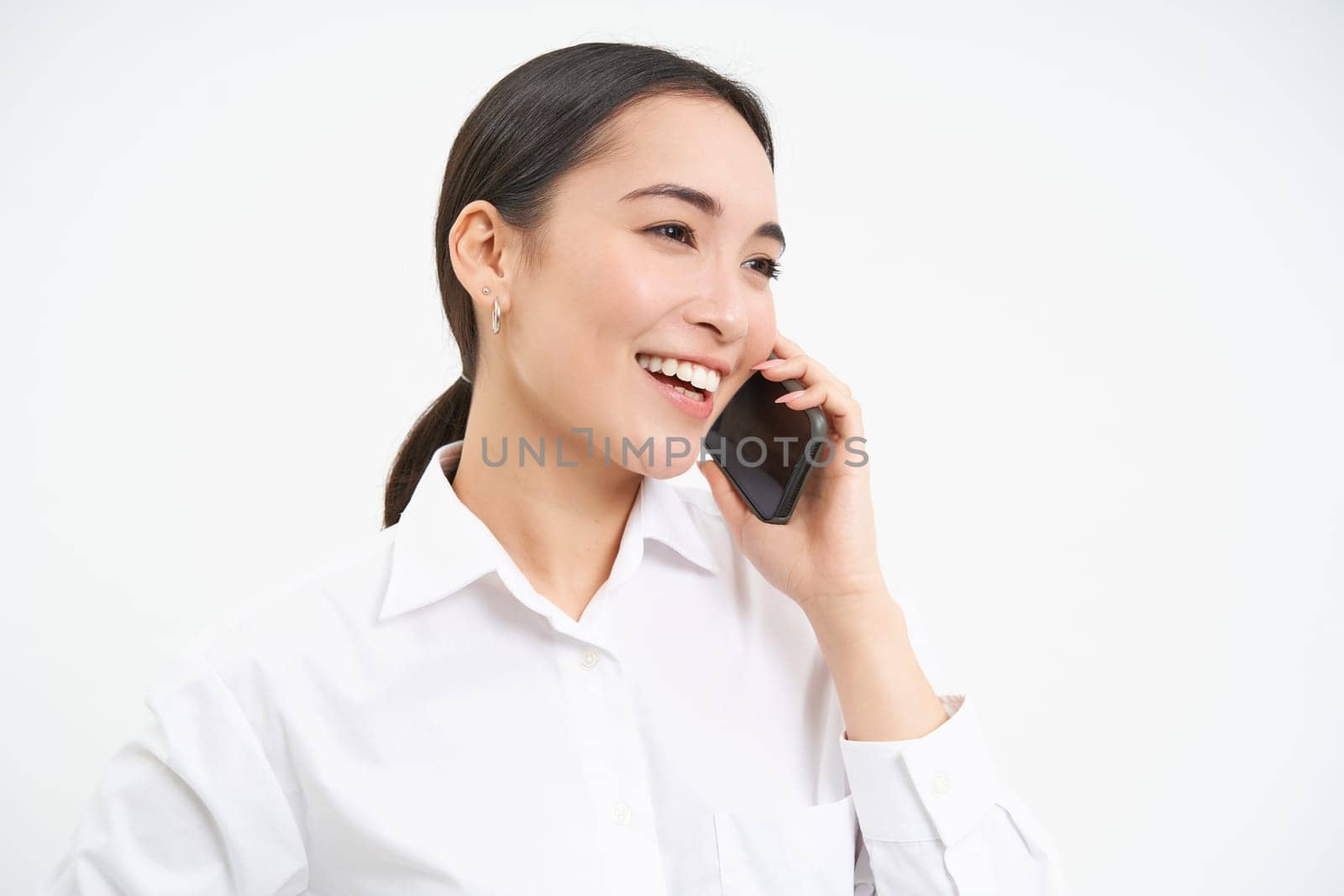 Portrait of asian corporate woman, businesswoman talks on mobile phone, has conversation over cellphone, speaking on telephone, white background by Benzoix