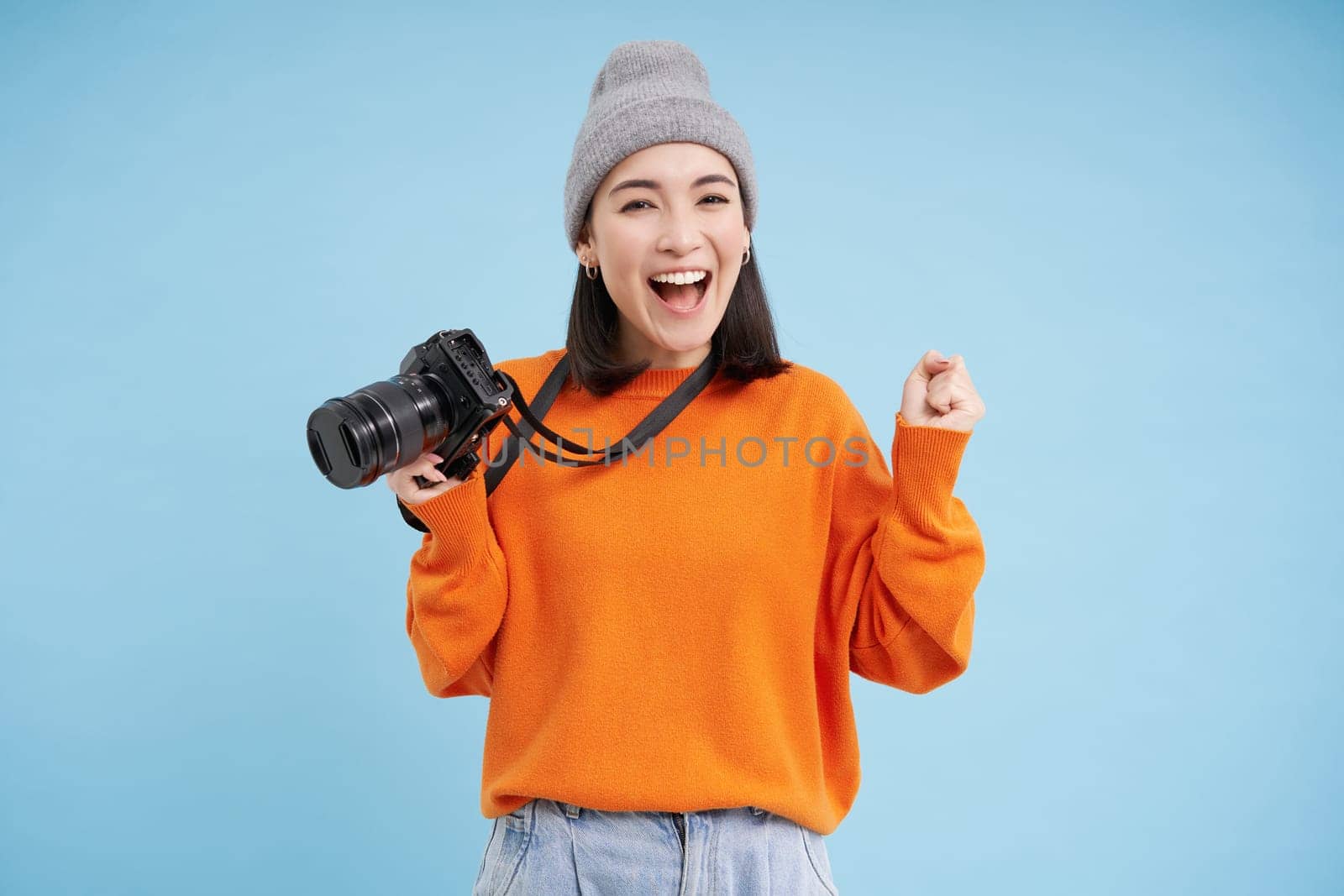 Stylish asian girl with digital camera, taking pictures. Woman photographer smiling, standing over blue background by Benzoix