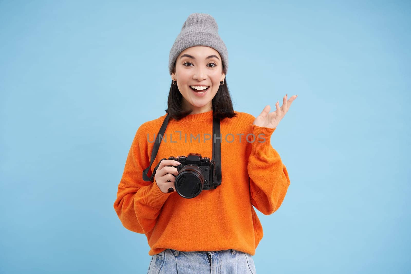 Stylish asian girl with digital camera, taking pictures. Woman photographer smiling, standing over blue background by Benzoix