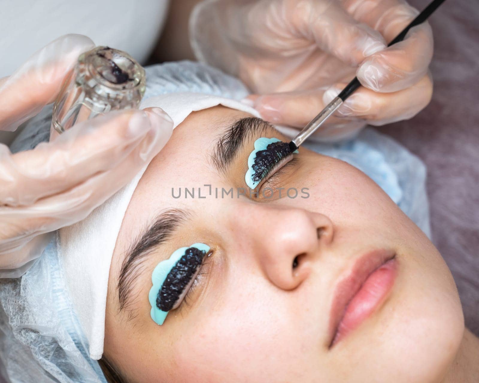 Close-up portrait of a woman on eyelash lamination procedure. The master applies tint to the eyelashes. by mrwed54