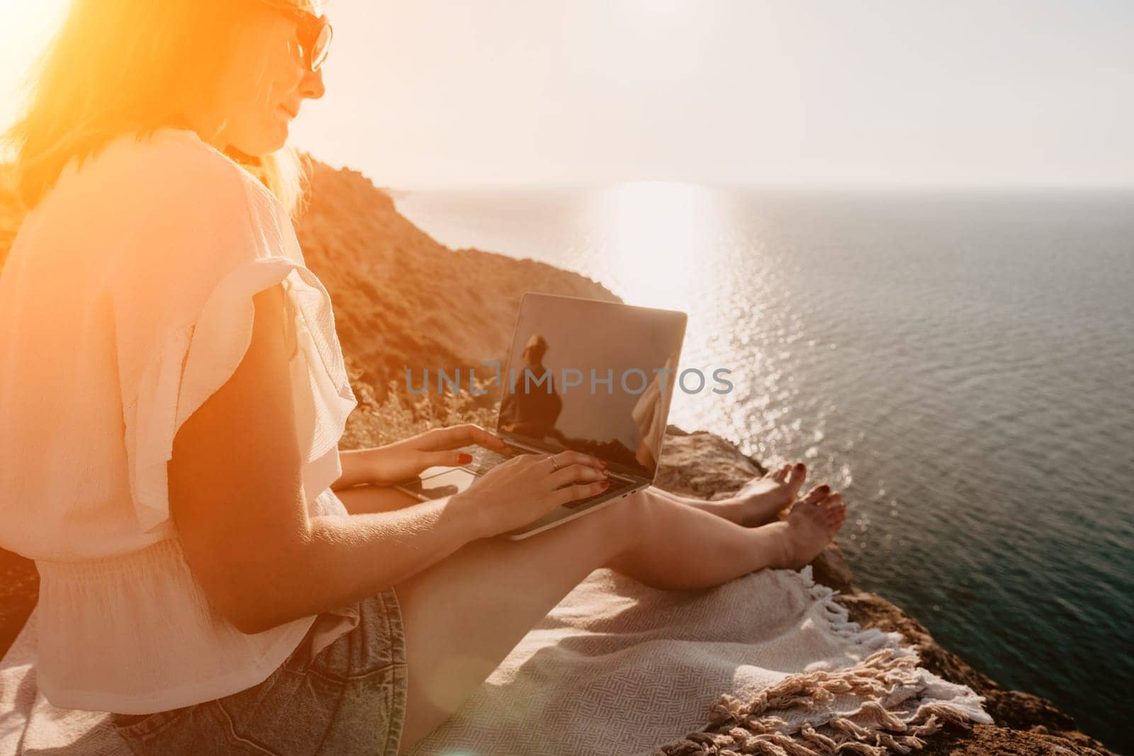 Woman sea laptop. Business woman in yellow hat working on laptop by sea. Close up on hands of pretty lady typing on computer outdoors summer day. Freelance, digital nomad, travel and holidays concept.