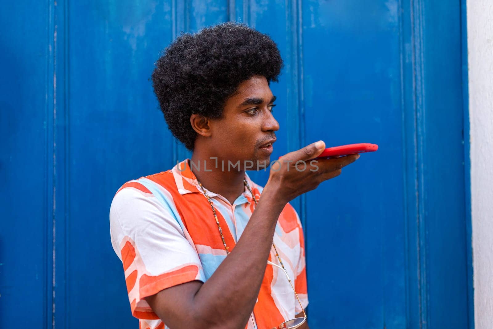African American man using cell phone to send voice message. Young black man with afro hairstyle talking on the phone. Copy space. Technology concept.