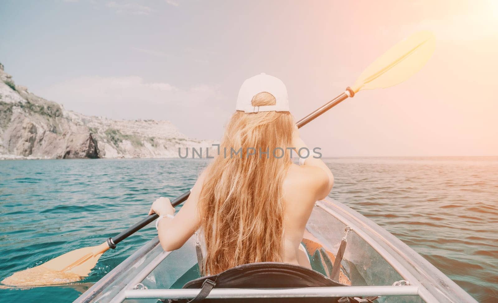 Woman in kayak back view. Happy young woman with long hair floating in transparent kayak on the crystal clear sea. Summer holiday vacation and cheerful female people having fun on the boat.