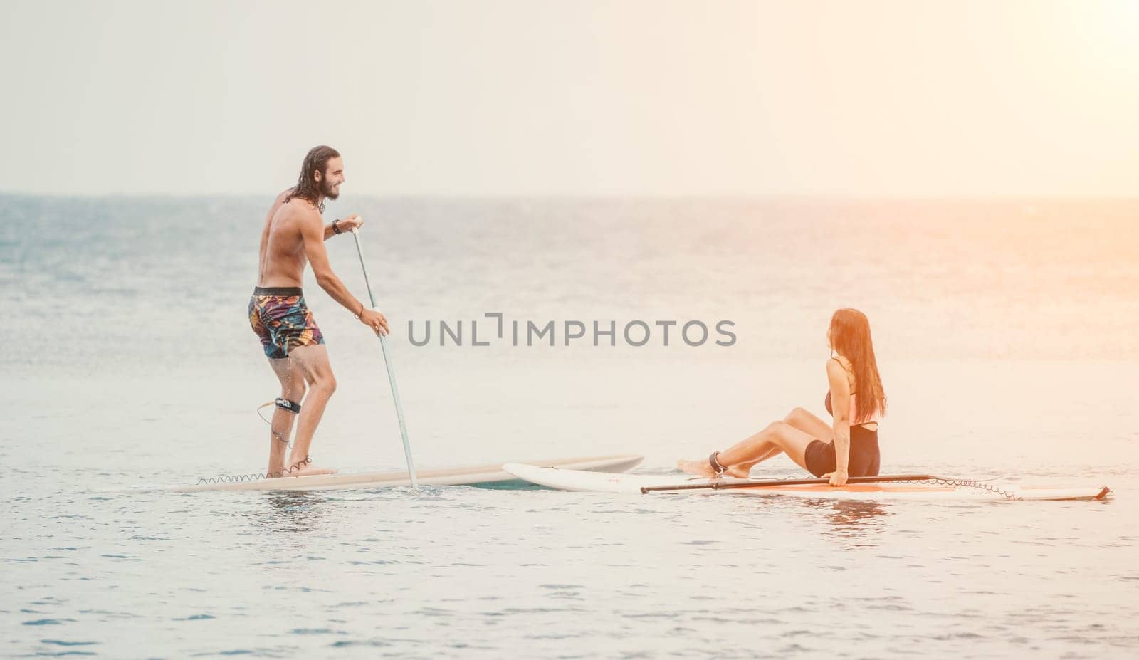 Sea woman and man on sup. Silhouette of happy young woman and man, surfing on SUP board, confident paddling through water surface. Idyllic sunset. Active lifestyle at sea or river