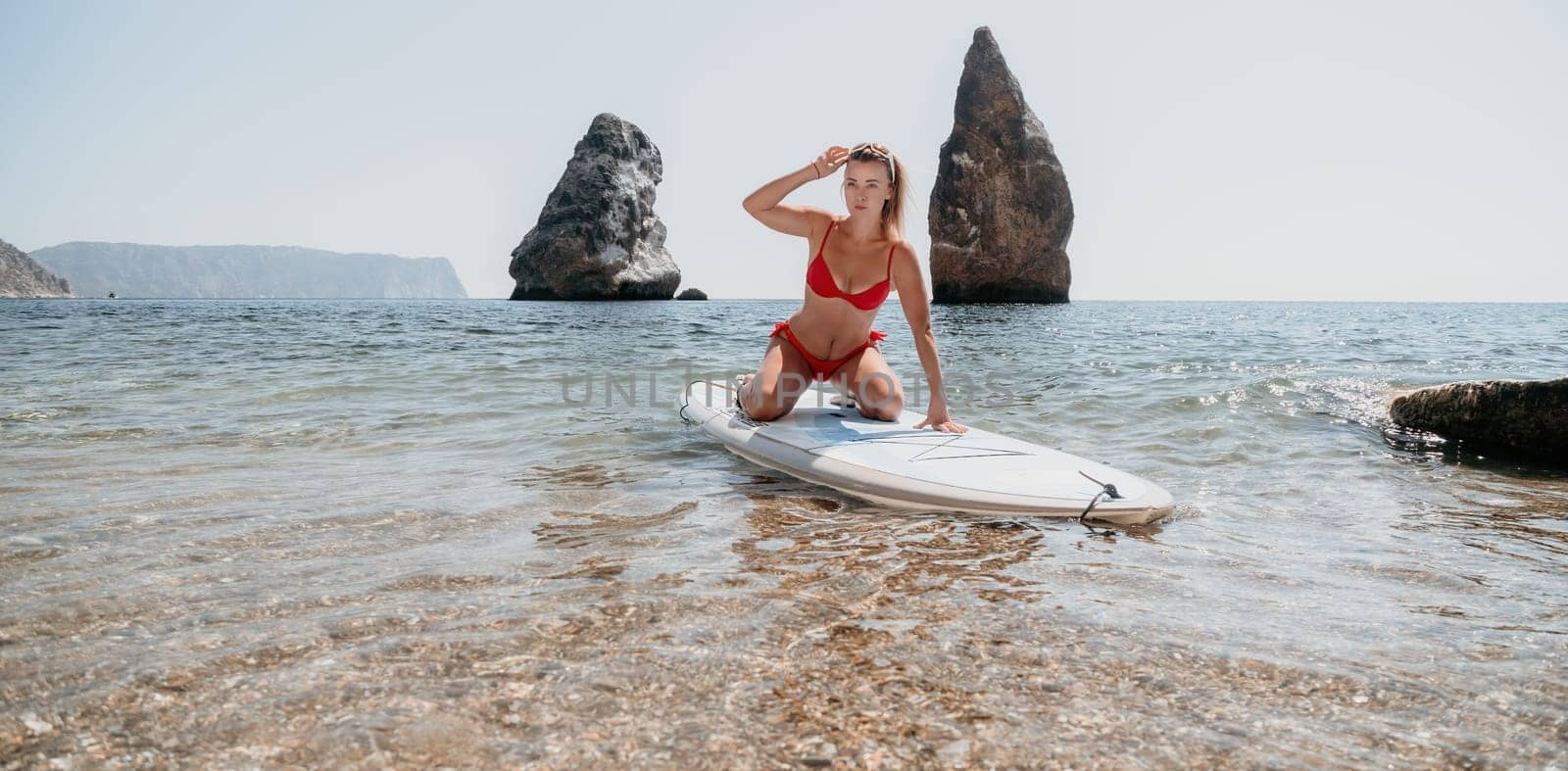 Woman sea sup. Close up portrait of happy young caucasian woman with blond hair looking at camera and smiling. Cute woman portrait in red bikini posing on sup board in the sea by panophotograph