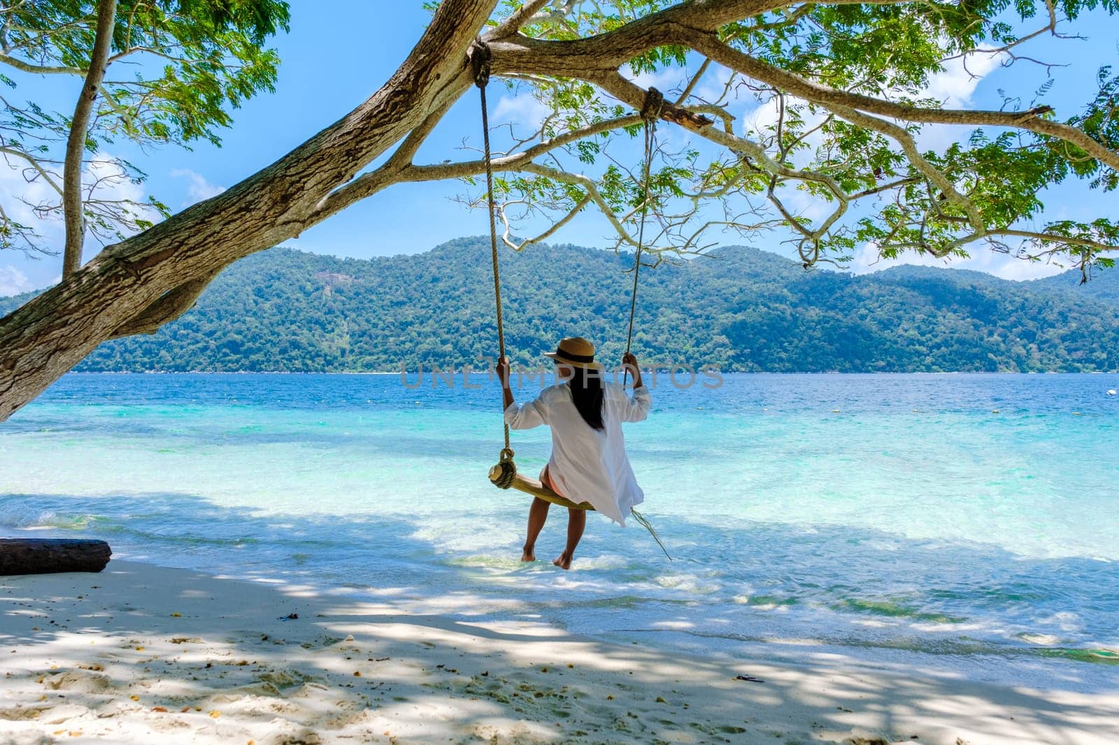woman swinging around under a tree at a swing on the beach of Koh Lipe Island Southern Thailand with turqouse colored ocean and white sandy beach at Ko Lipe. Tarutao National Park, Koh Rawi Island