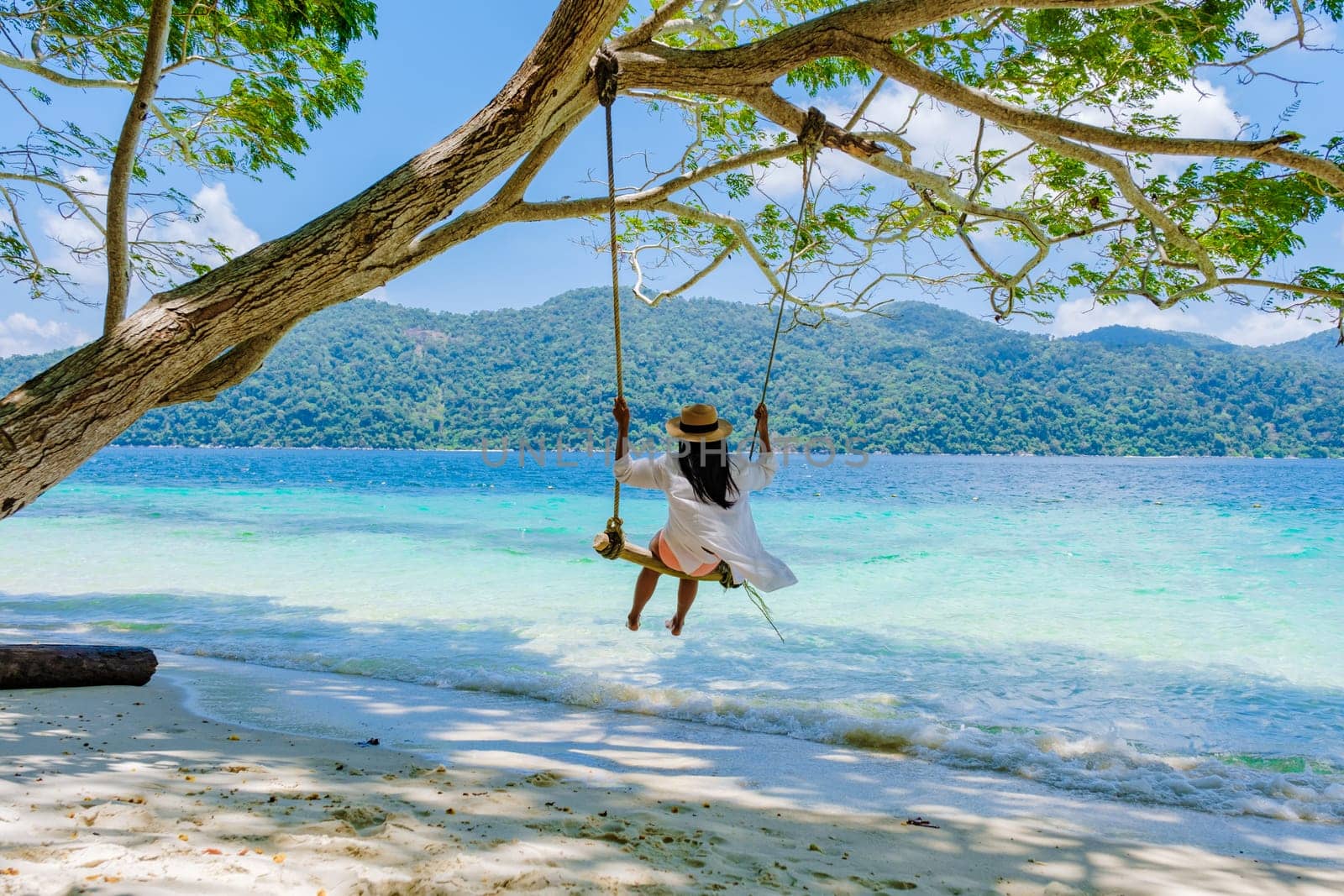 woman swinging around under a tree at a swing on the beach of Koh Lipe Island Southern Thailand with turqouse colored ocean and white sandy beach at Ko Lipe. Tarutao National Park, Koh Rawi Island