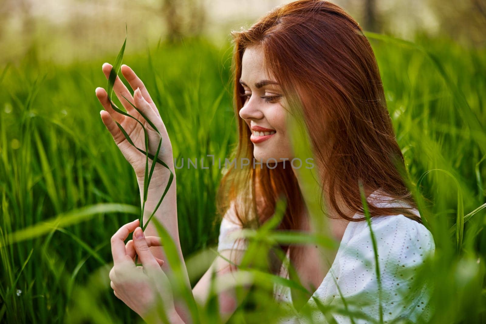 portrait of a blissfully smiling woman sitting in the grass with a leaf in her hand by Vichizh