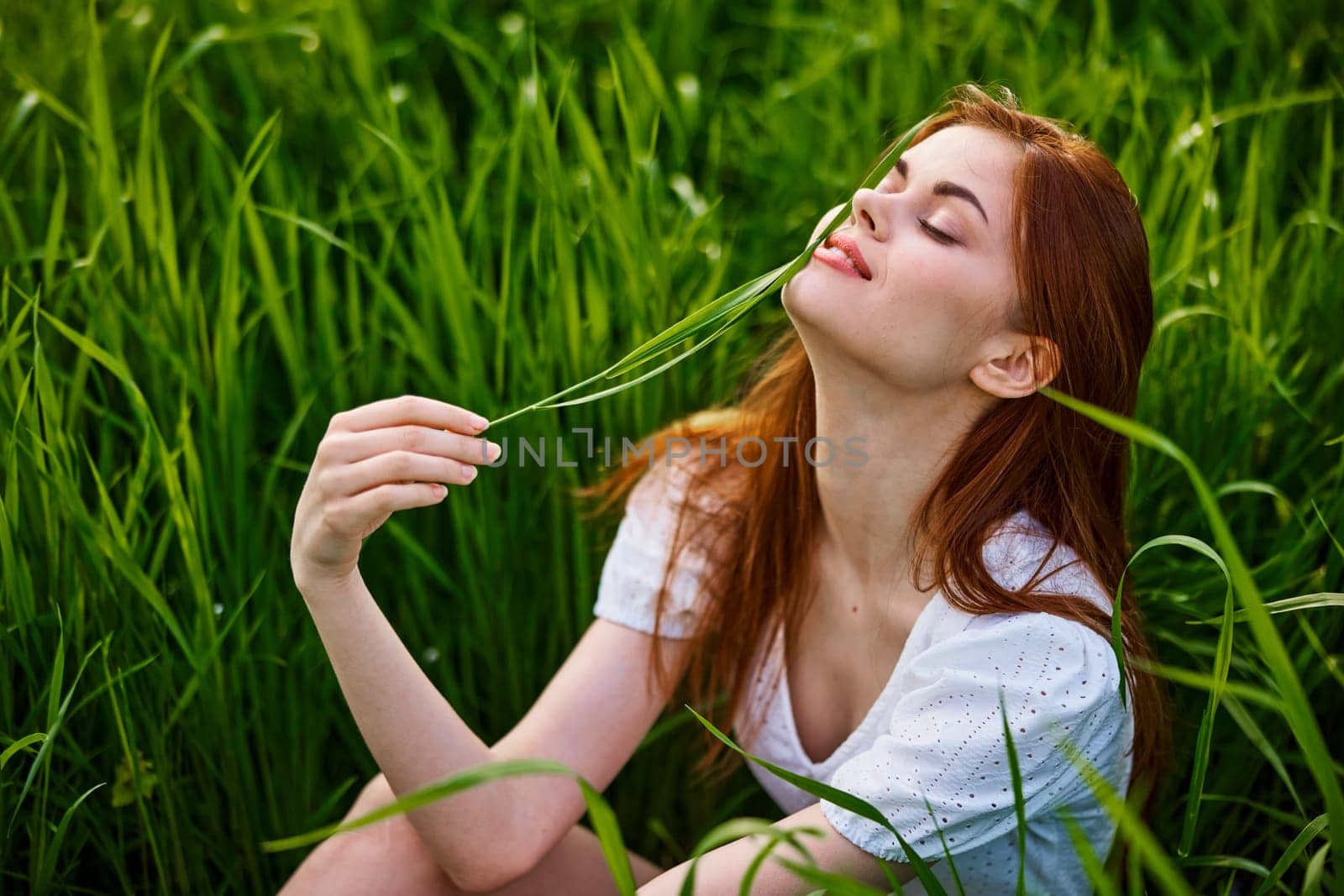 portrait of a beautiful redhead woman sitting in the grass on a sunny day at sunset. High quality photo