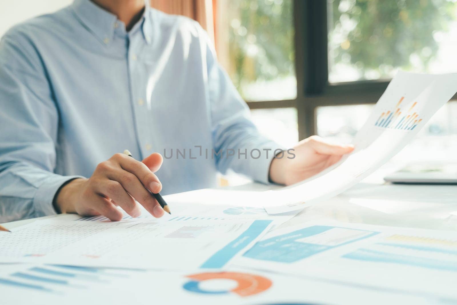 Close-up of businessmen working together at workplace, discussing about strategies, plans, analytic progress, and financial stats, and pointing at graph documents on desk holding pencils. Business and Teamwork concept.