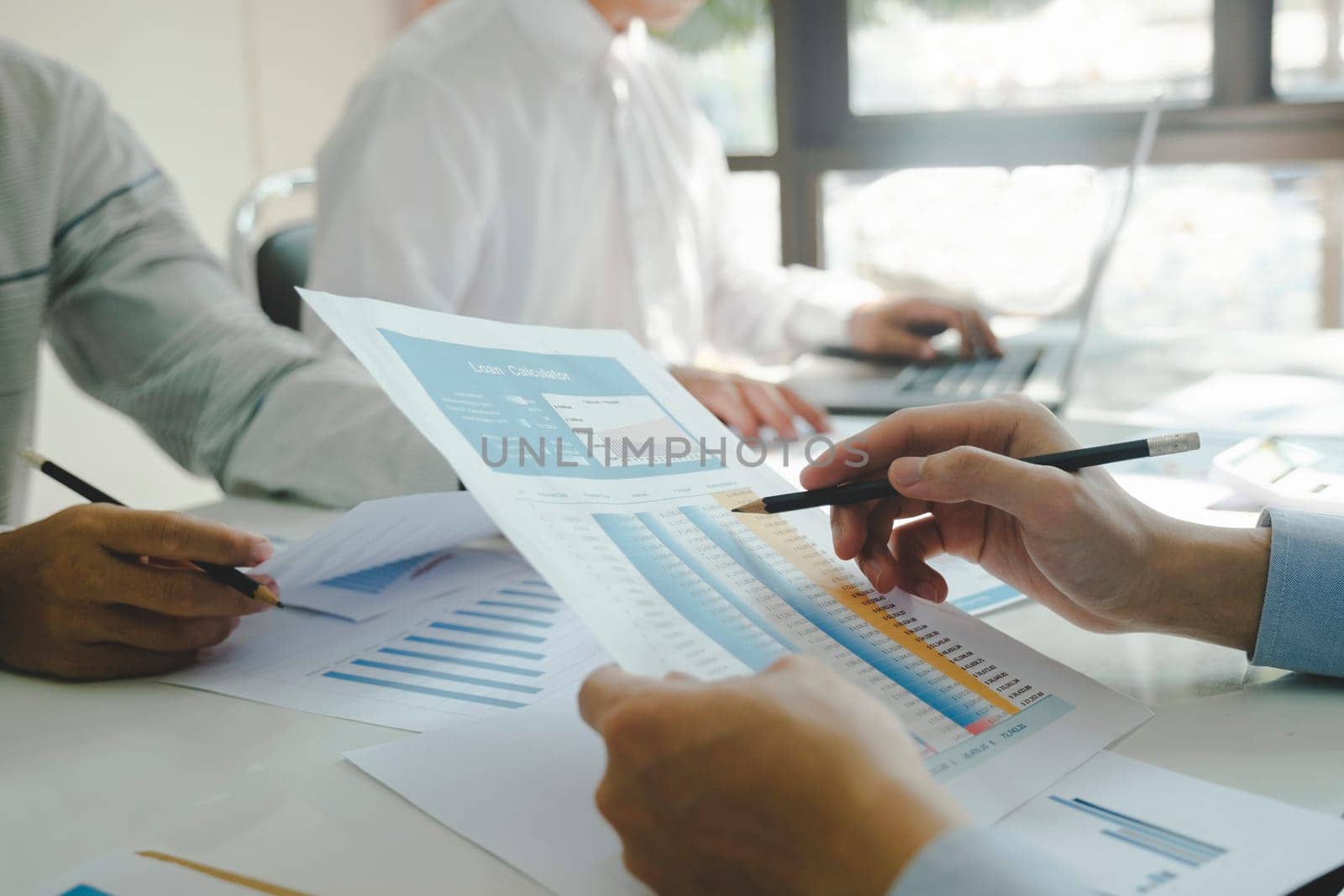 Close-up of businessmen working together at workplace, discussing about strategies, plans, analytic progress, and financial stats of company, and pointing at graph documents on desk with laptop holding pencils. Business and Teamwork concept.