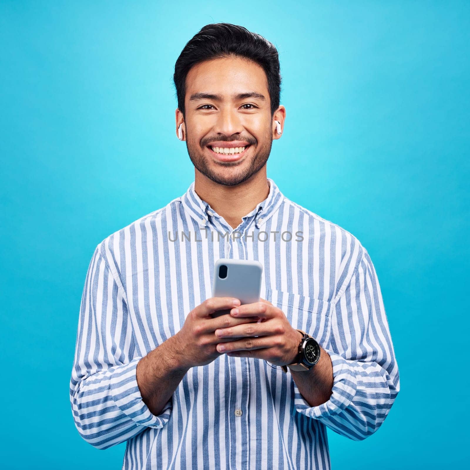 Happy, portrait and a man with a phone for communication isolated on a blue background in a studio. Smile, social media update and a person typing on a mobile for app, notification reply and message.