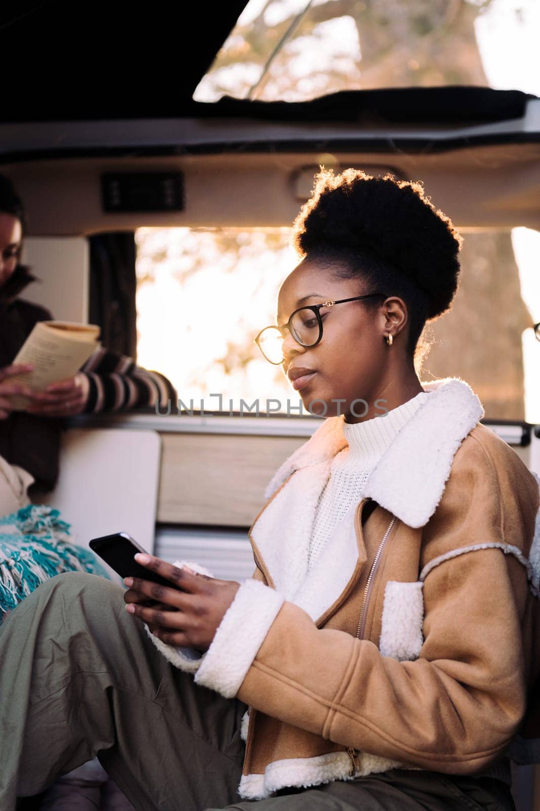young african woman in camper van checking phone, concept of adventure travel and technology of communication