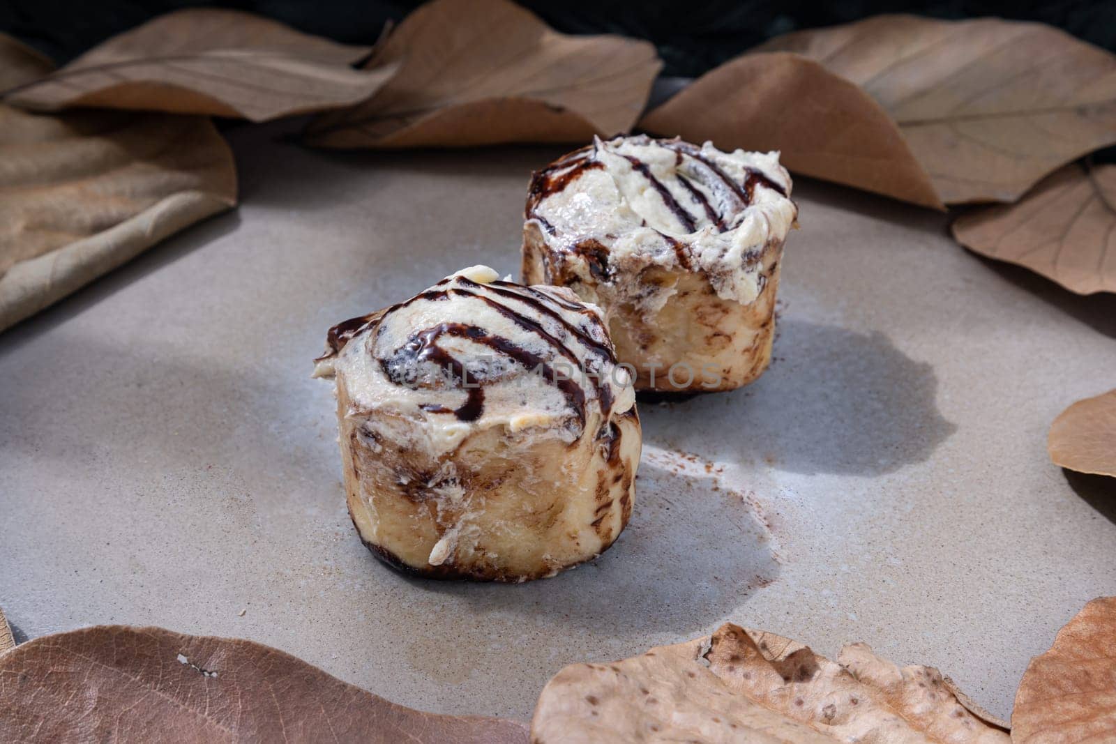 Two Soft Chocolate Buns topped with rich cream cheese frosting on ceramic tray with dark background. The concept of delicious food, Space for text, Selective Focus.