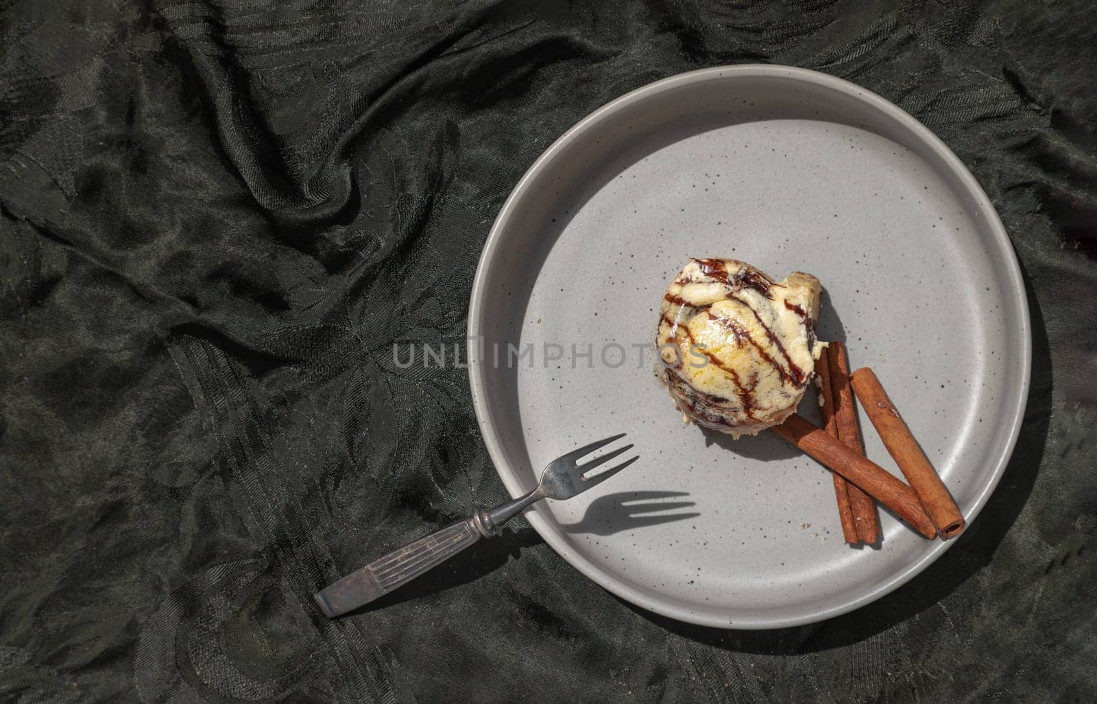 Chocobon (Soft chocolate bun) topped with rich cream cheese frosting and Cinnamon served with Metal fork on ceramic plate with dark background. Top view, Space for text, Selective focus.
