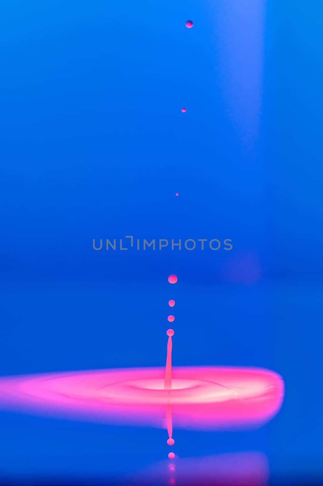 A drop falls into a thick liquid with a blue-pink background. Abstract colorful background