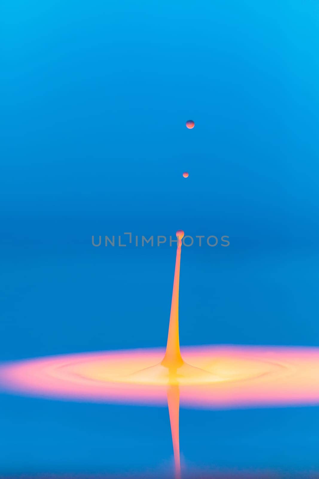 A drop falls into a thick liquid with a blue-yellow background. Abstract colorful background
