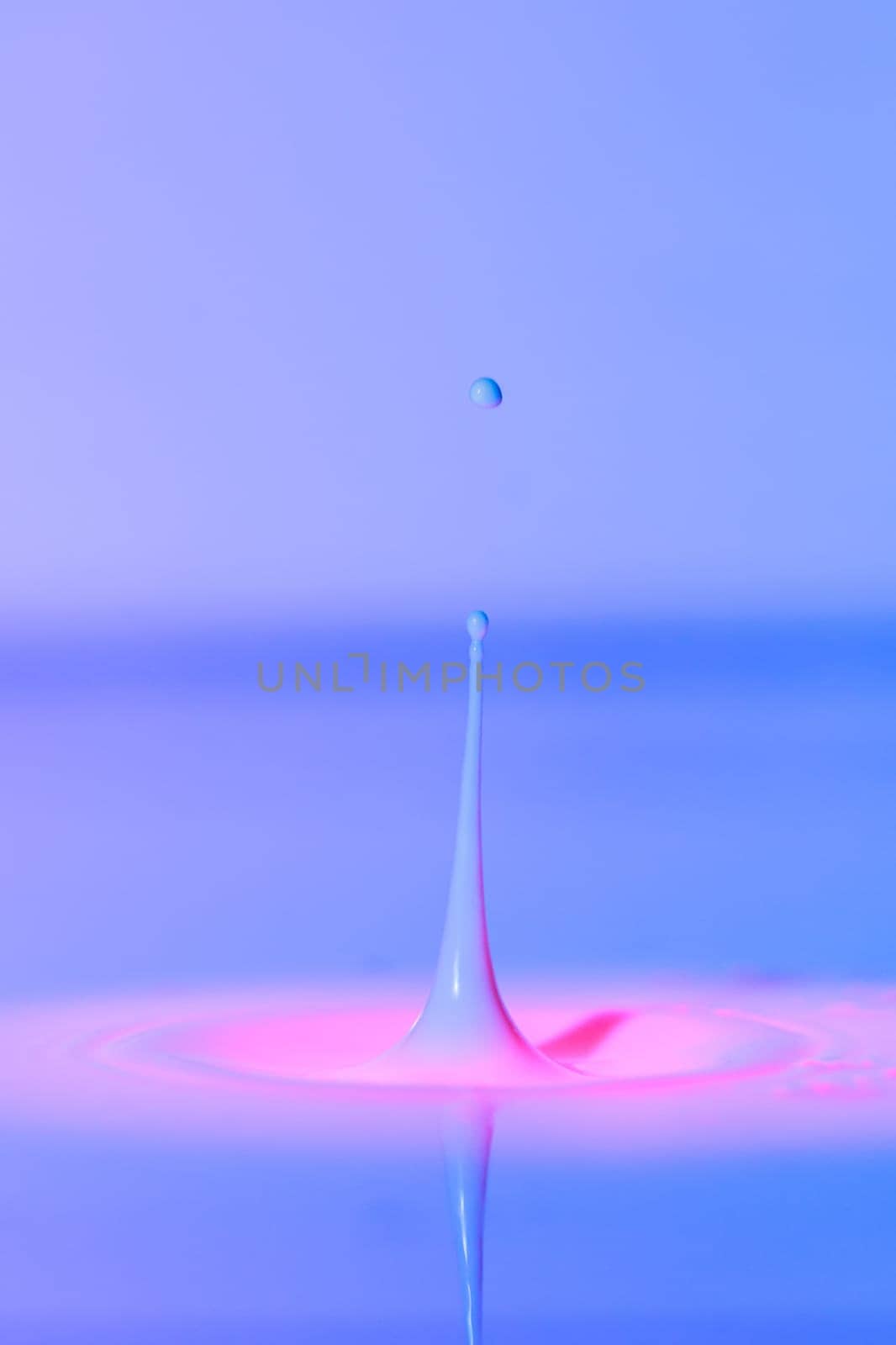 A drop falls into a thick liquid with a blue-pink background. Abstract colorful background