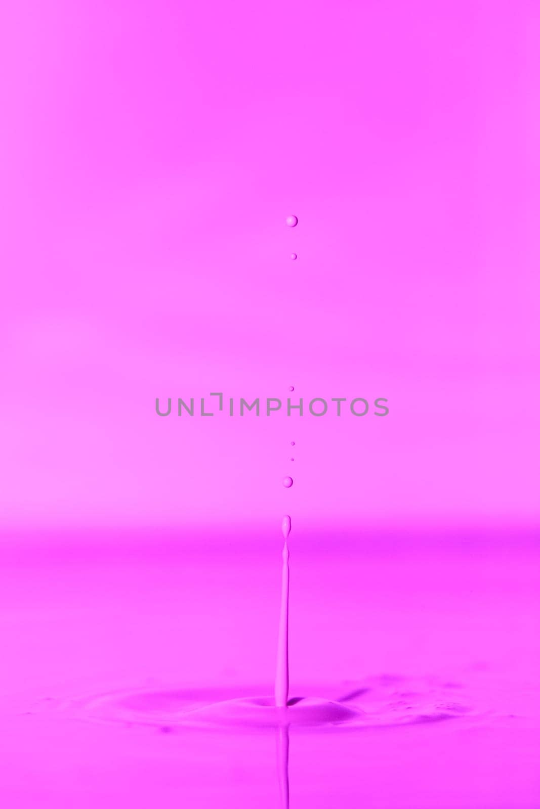 A drop falls into a thick liquid with a pink background. Abstract colorful background