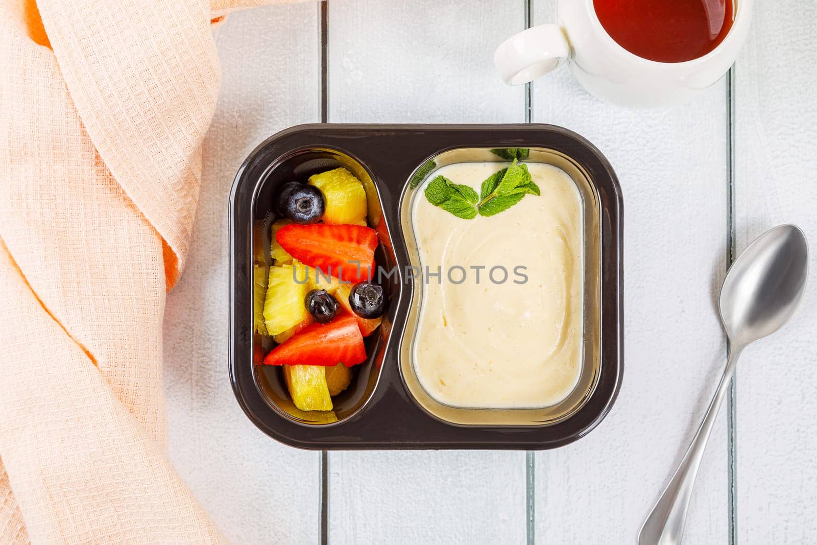 Dessert of applesauce, pineapple and strawberries in a plastic container on a wooden background. High quality photo