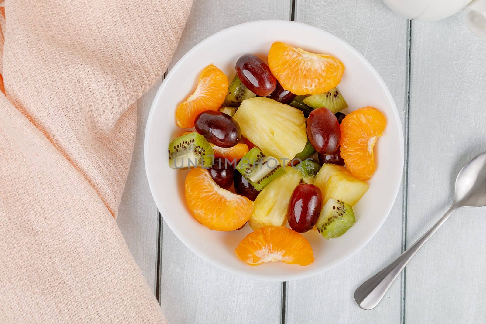 Fruit salad of pineapple, orange, kiwi and grapes in a plate on a wooden background. High quality photo