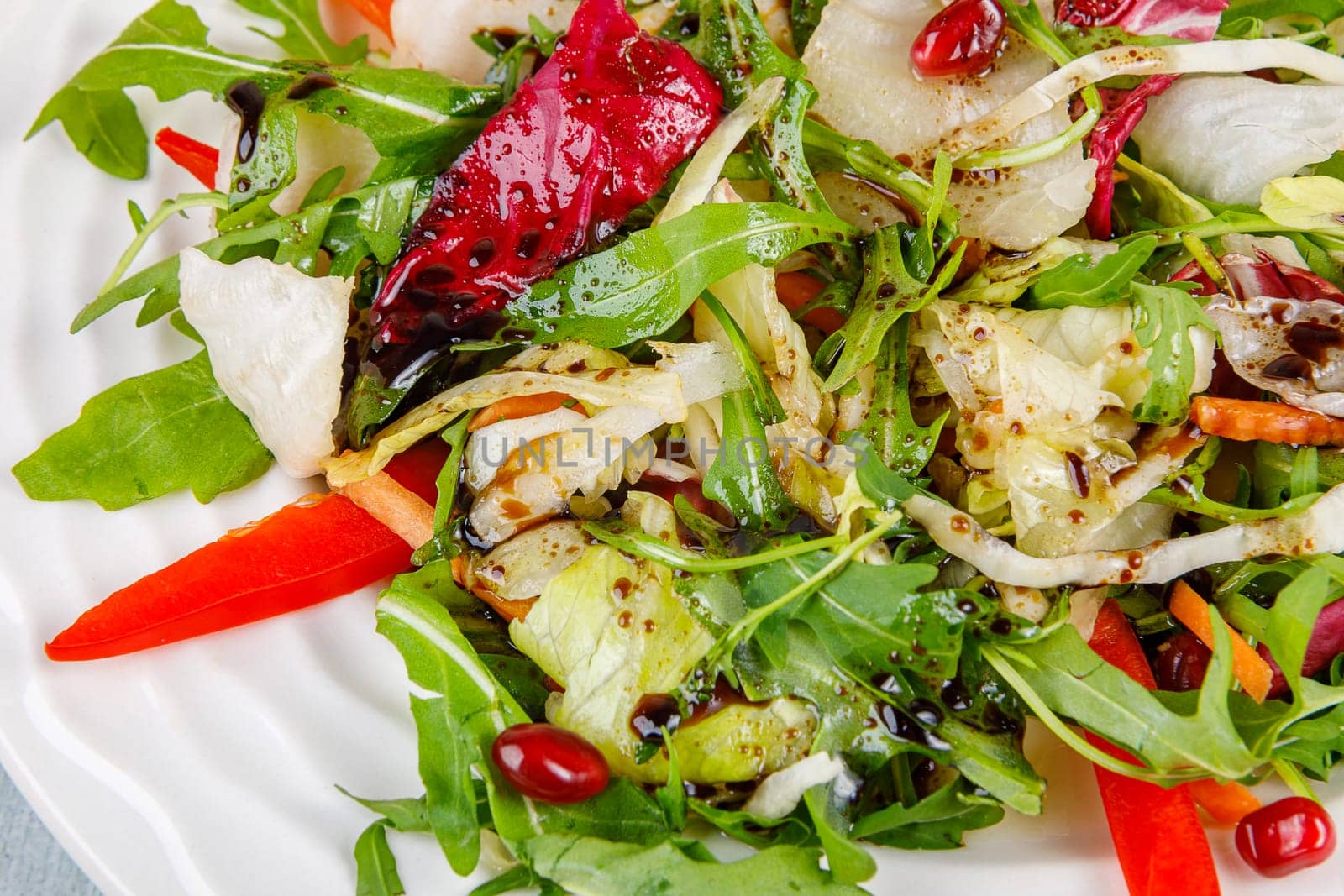 Fresh salad of cabbage, herbs, peppers, carrots and pomegranate seeds in a white plate. High quality photo