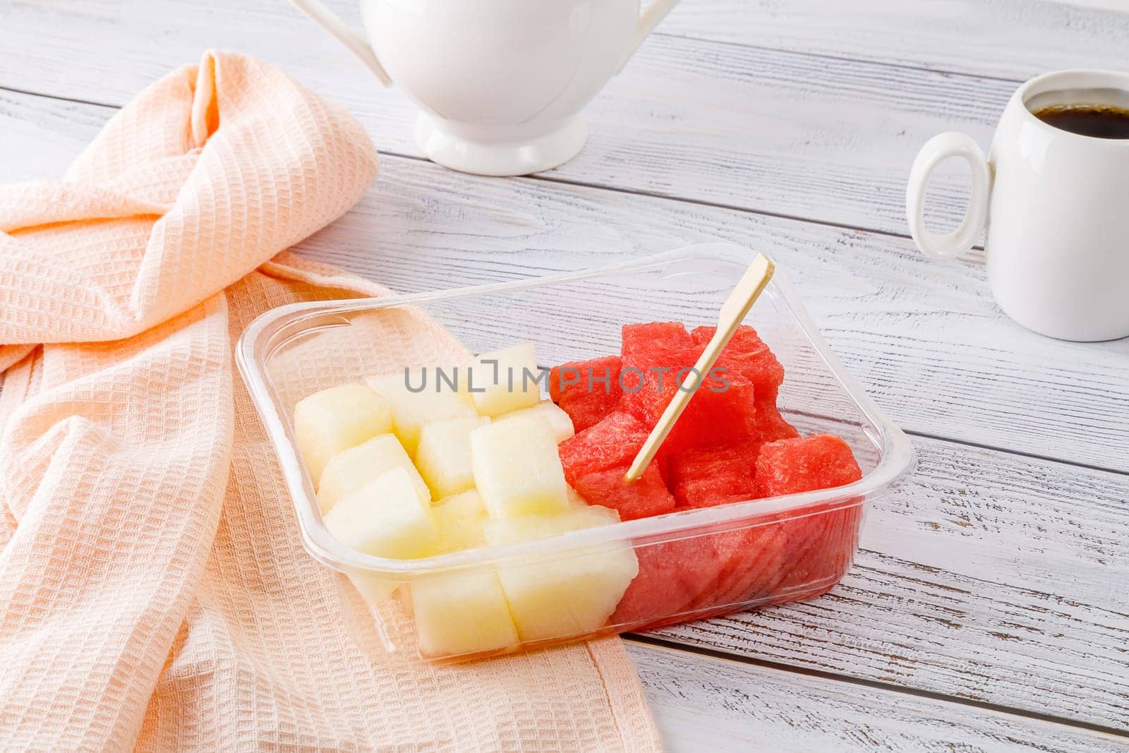 Fruit salad with watermelon and melon in a plastic container on a wooden background. High quality photo
