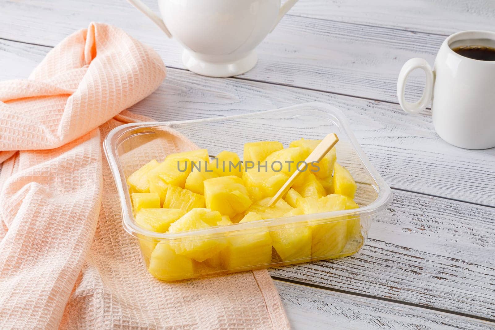 Pineapple fruit salad in a plastic container on a wooden background. High quality photo