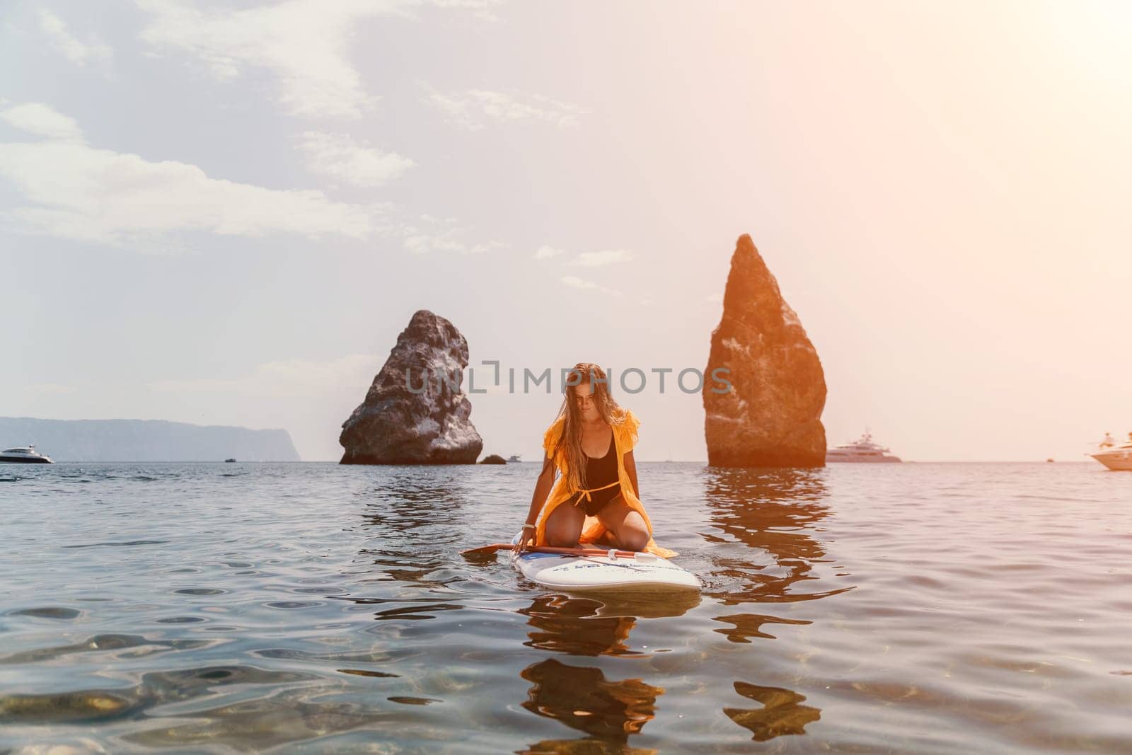 Close up shot of beautiful young caucasian woman with black hair and freckles looking at camera and smiling. Cute woman portrait in a pink bikini posing on a volcanic rock high above the sea