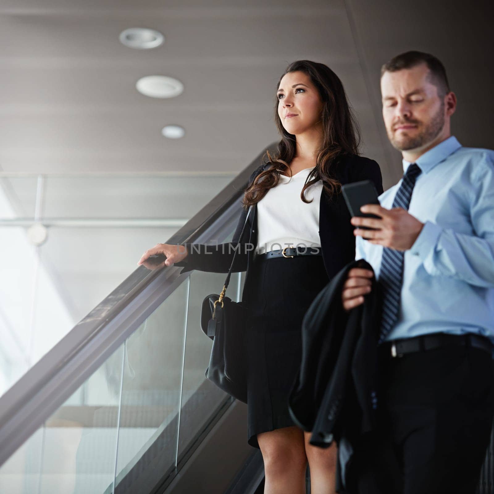 Working their way around the world. a businessman using a mobile phone while traveling down an escalator in an airport