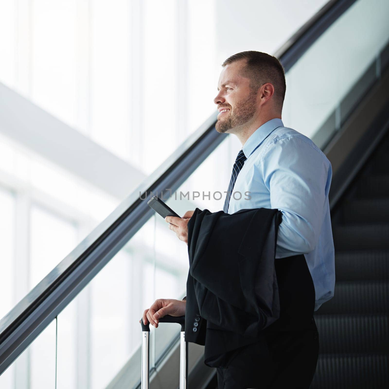 On the way to where the money is. a businessman traveling down an escalator in an airport. by YuriArcurs