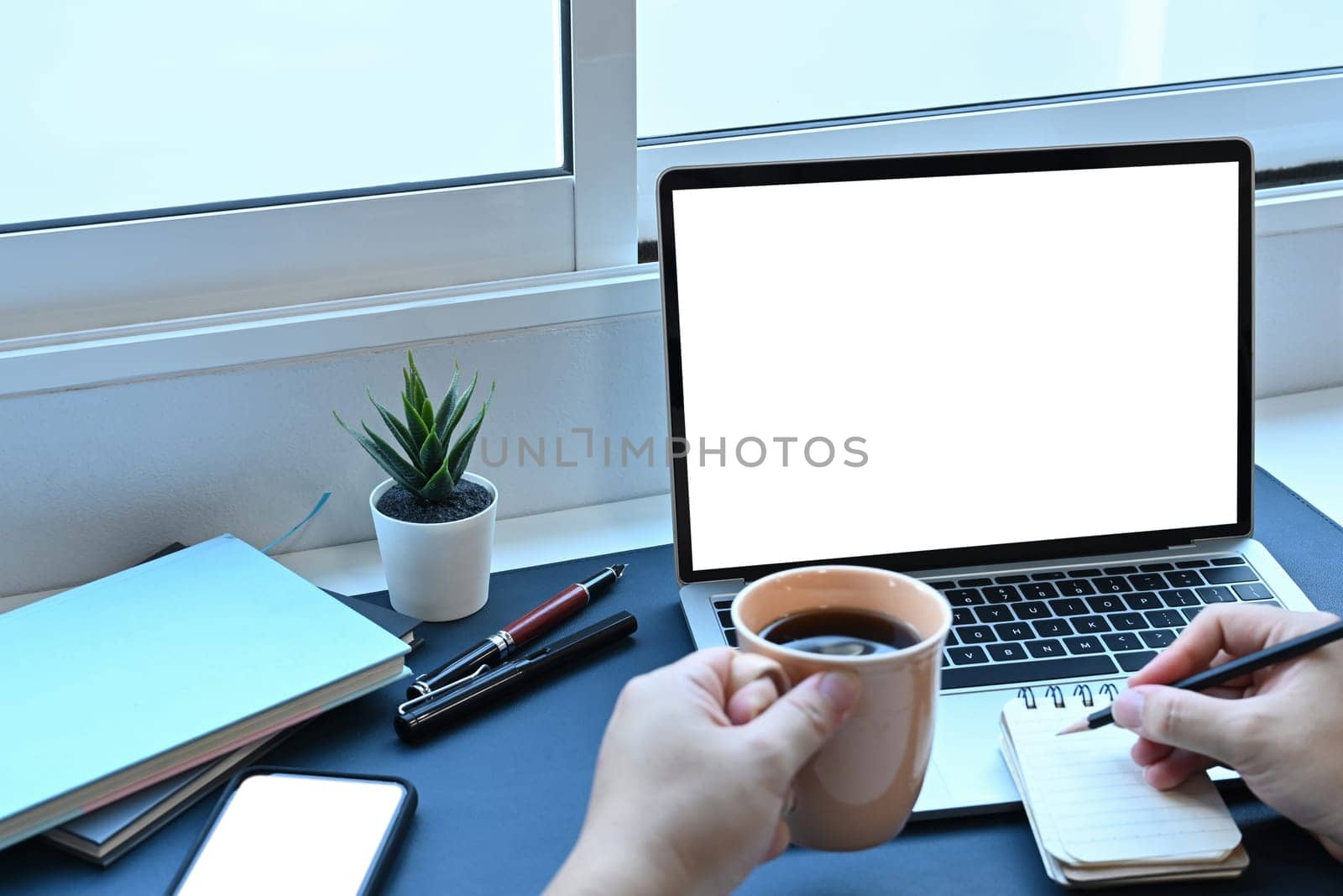 Man holding coffee cup and working with laptop computer at home.