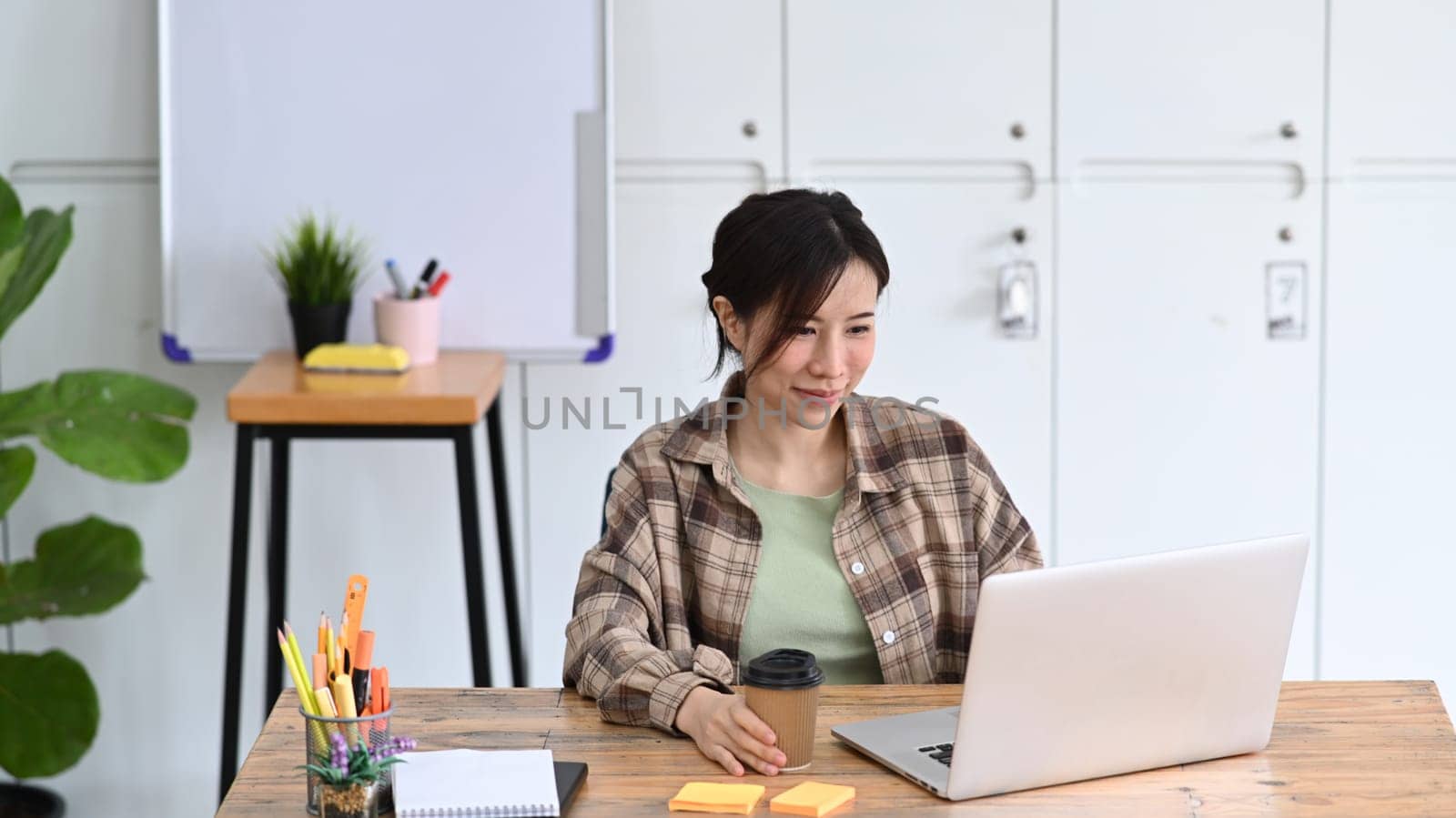 Smiling young woman designer working with laptop in modern workplace.