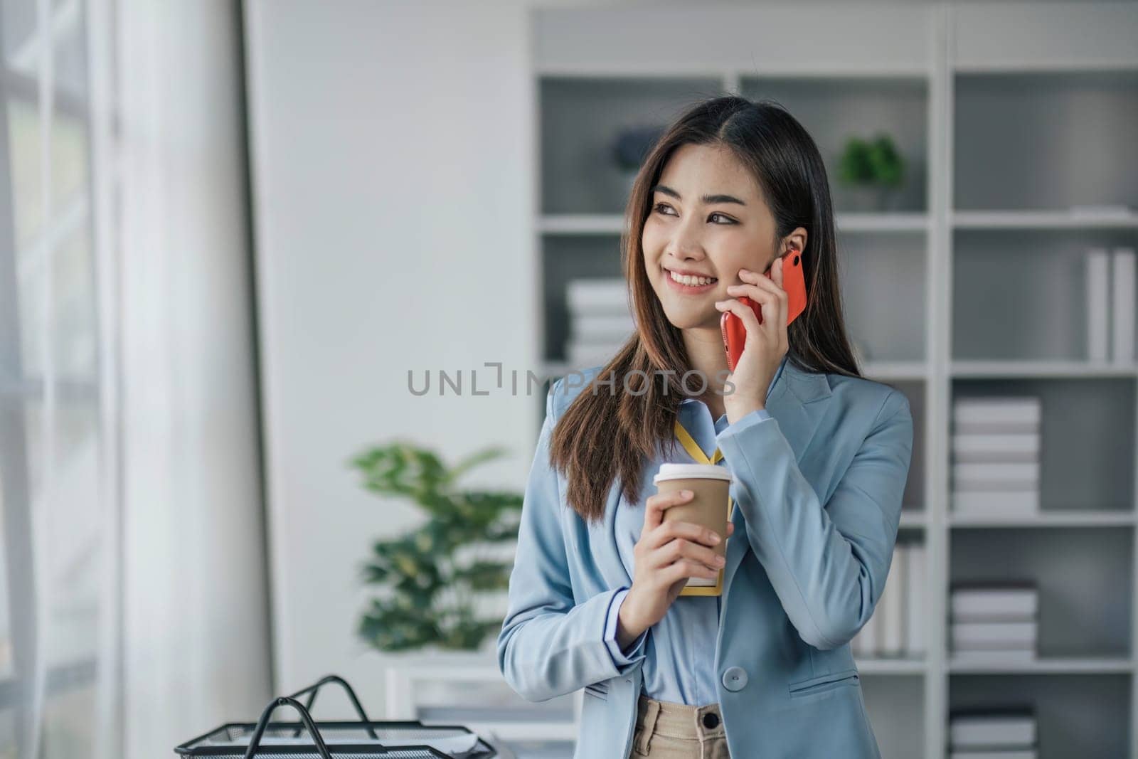 Pretty young Asian business woman standing talking on the phone in the office...