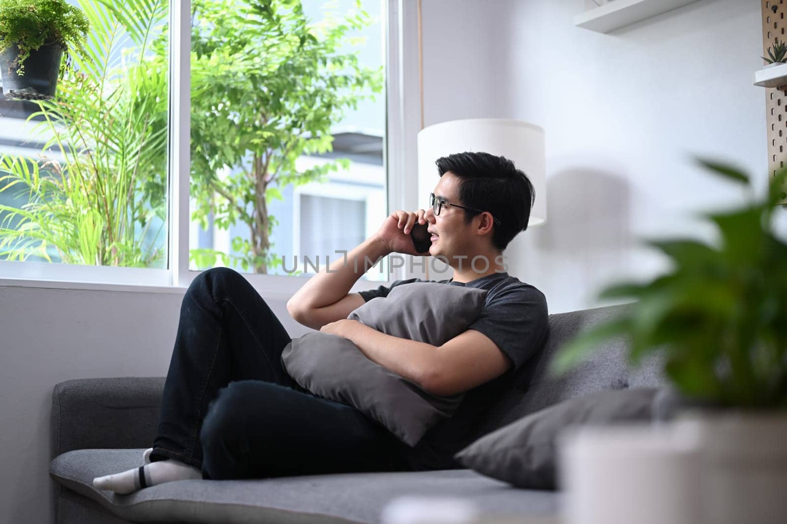 Young Asian man sitting on couch and talking on mobile phone.