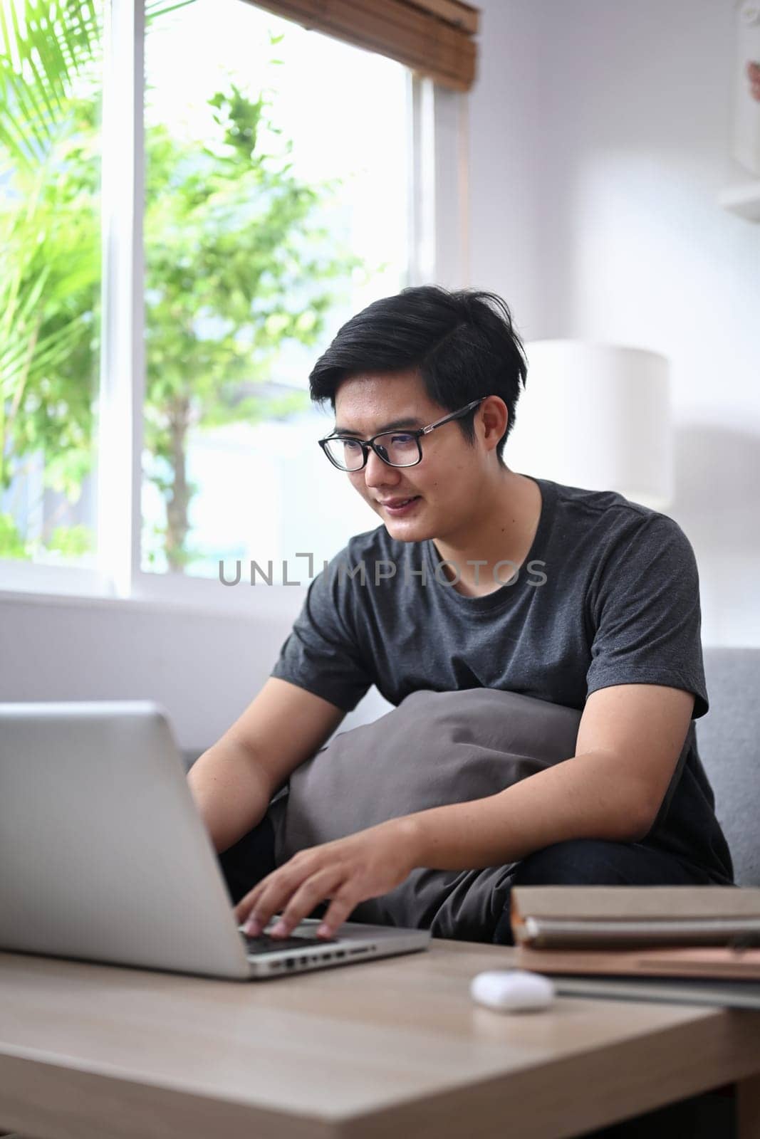 Smiling young man surfing internet with computer laptop in living room.