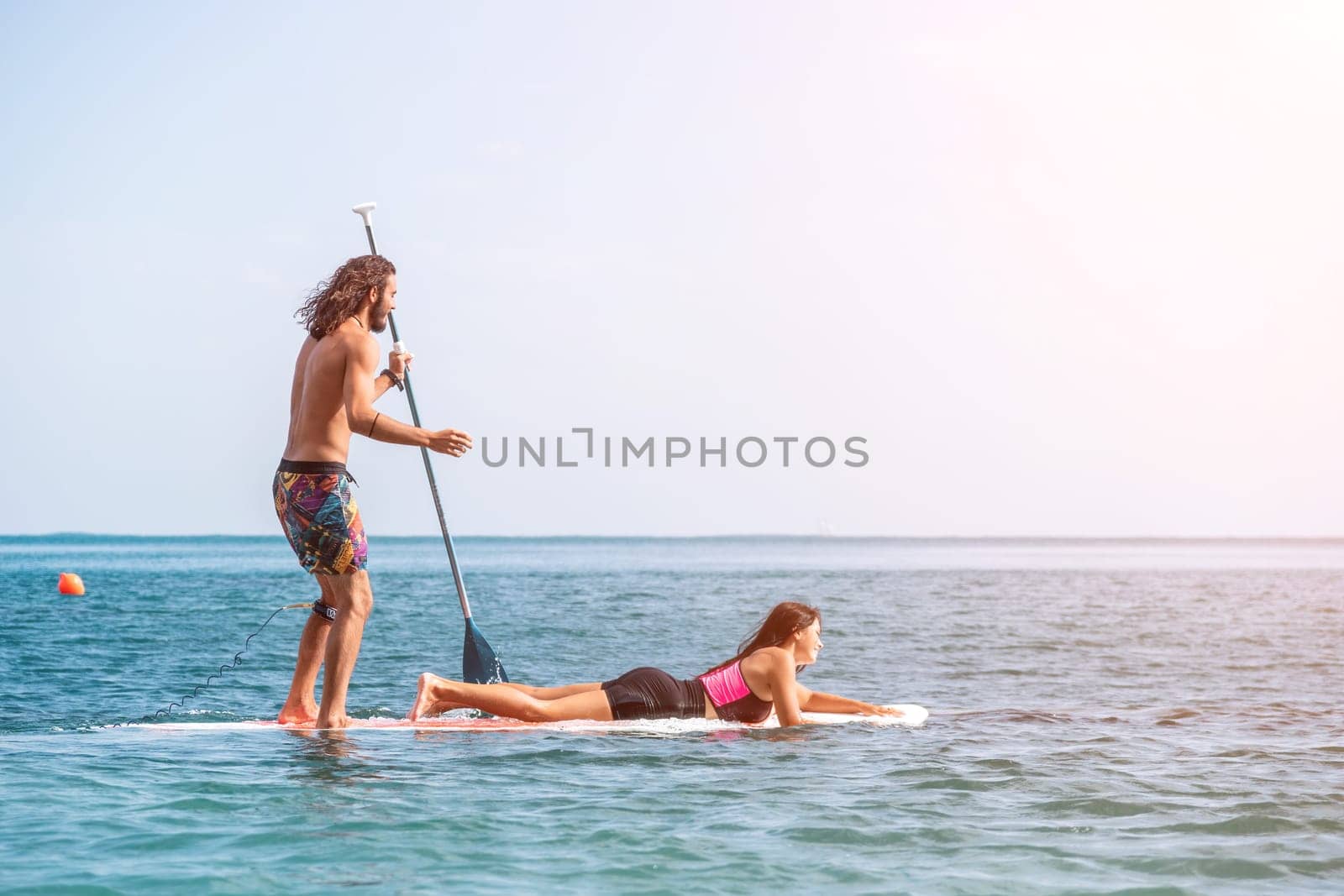 Silhouette of woman standing, surfing on SUP board, confident paddling through water surface. Idyllic sunset or sunrise. Sports active lifestyle at sea or river.