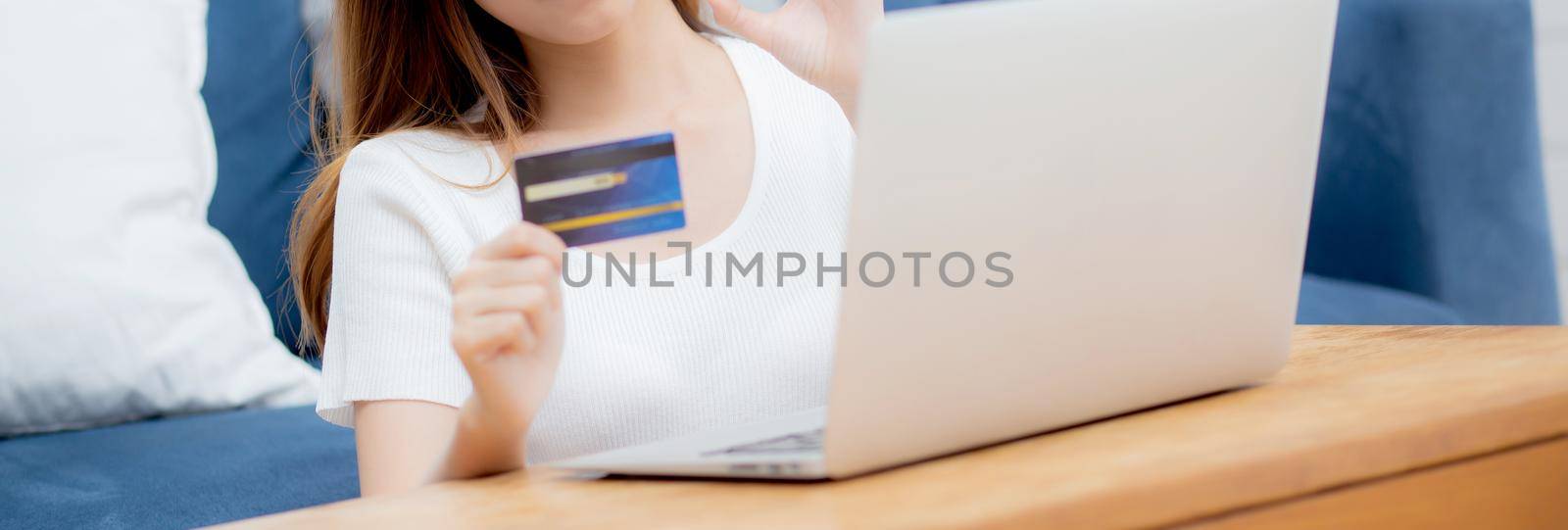 Young asian woman sit on sofa using laptop computer shopping online with credit card buying to internet, happy girl payment with e-commerce on couch, purchase and payment, business concept.