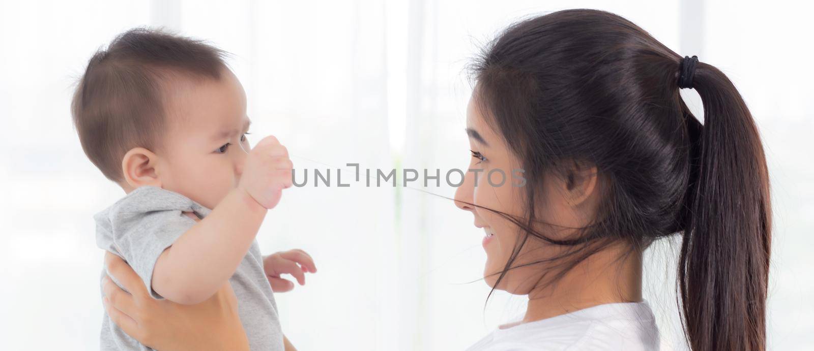 Young asian mother holding little baby girl together in the bedroom at home, mom carry child and care, woman and kid with carefree, toddler and parent, emotion and expression, family concept.