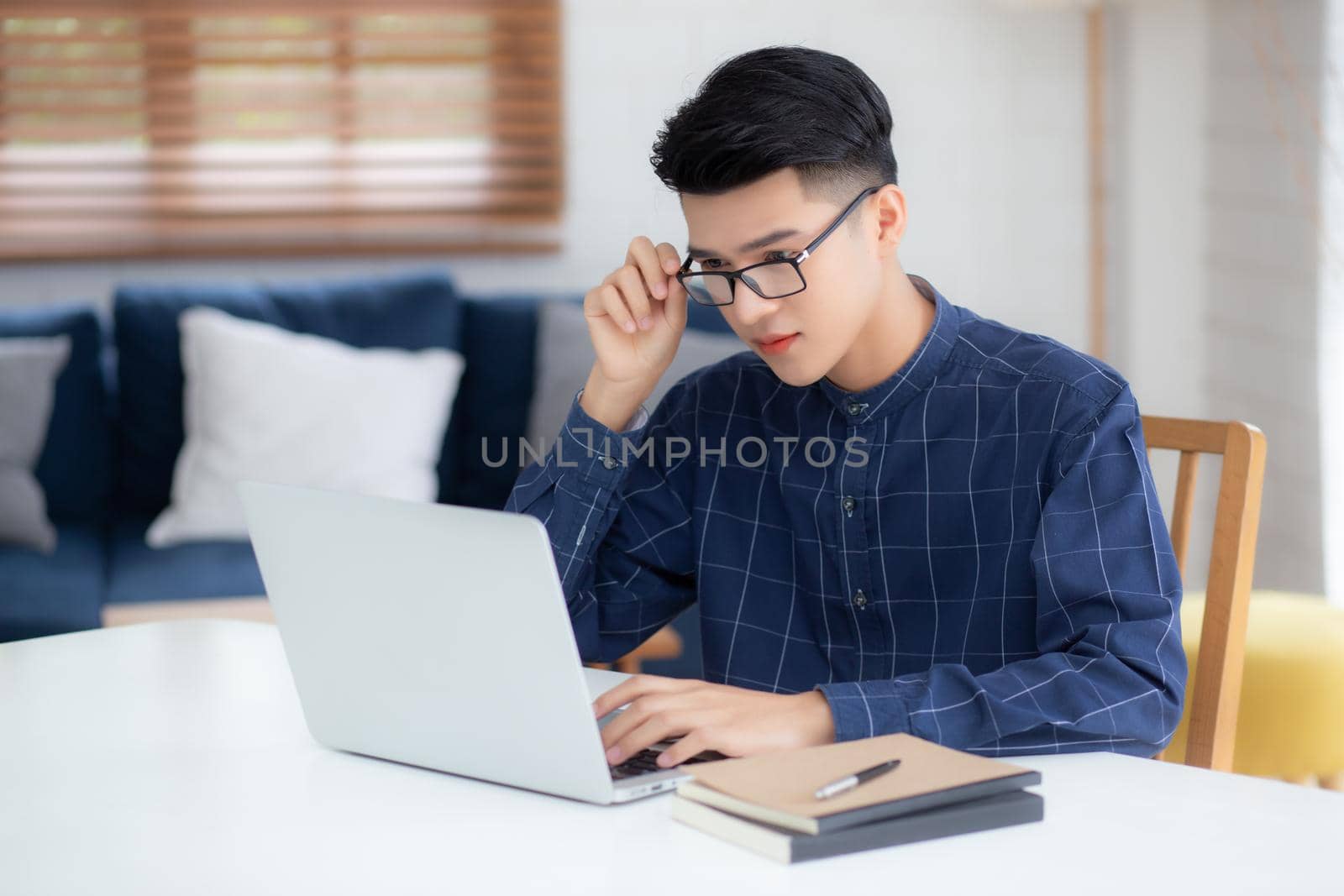 Young business man in glasses working from home with laptop computer on desk, freelance male sitting stay home using notebook for communication on table, entrepreneur in startup business, new normal. by nnudoo
