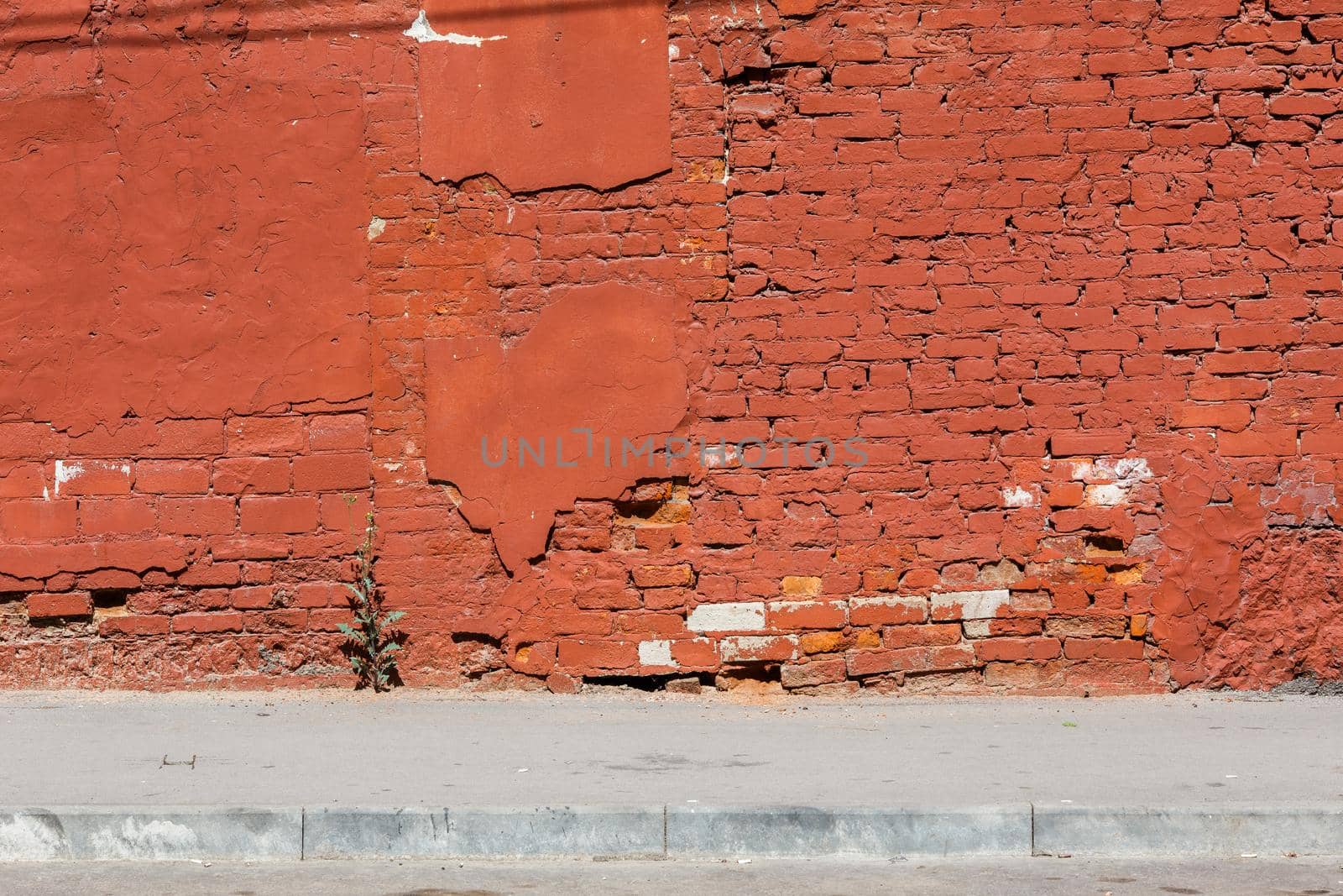 old brick wall with peeled off plaster, all over painted orange - background with sidewalk under it