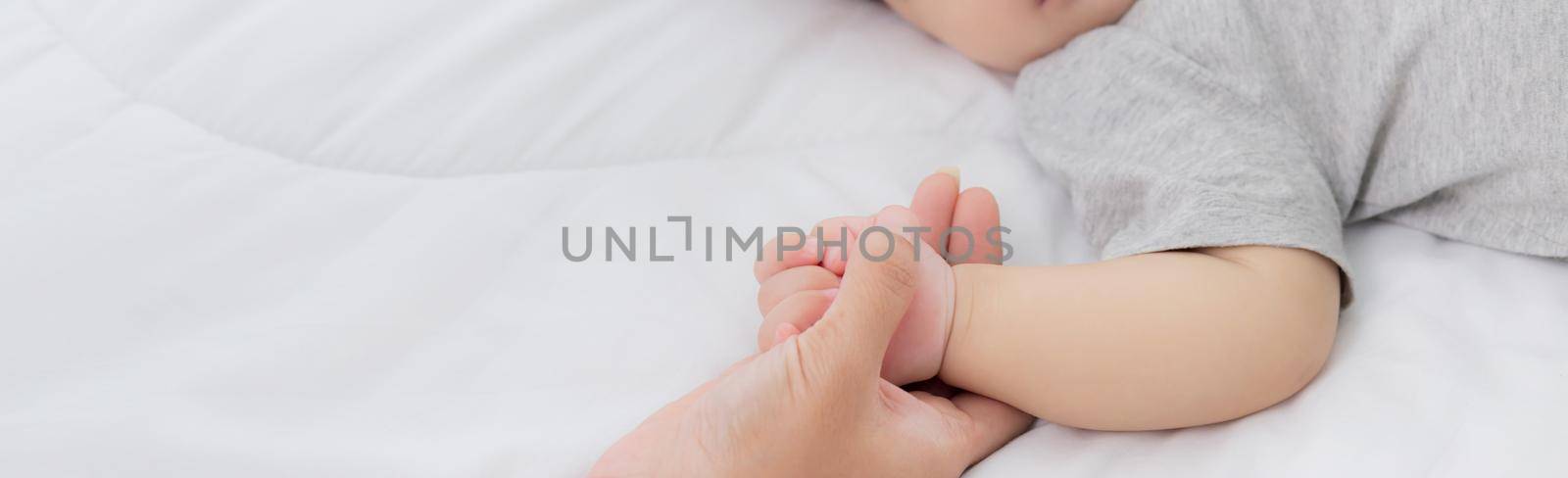 Young asian mother touch hand of little baby girl with tender on bed in the bedroom, mom love newborn and care, woman with expression with child together, parent and daughter, family concept.